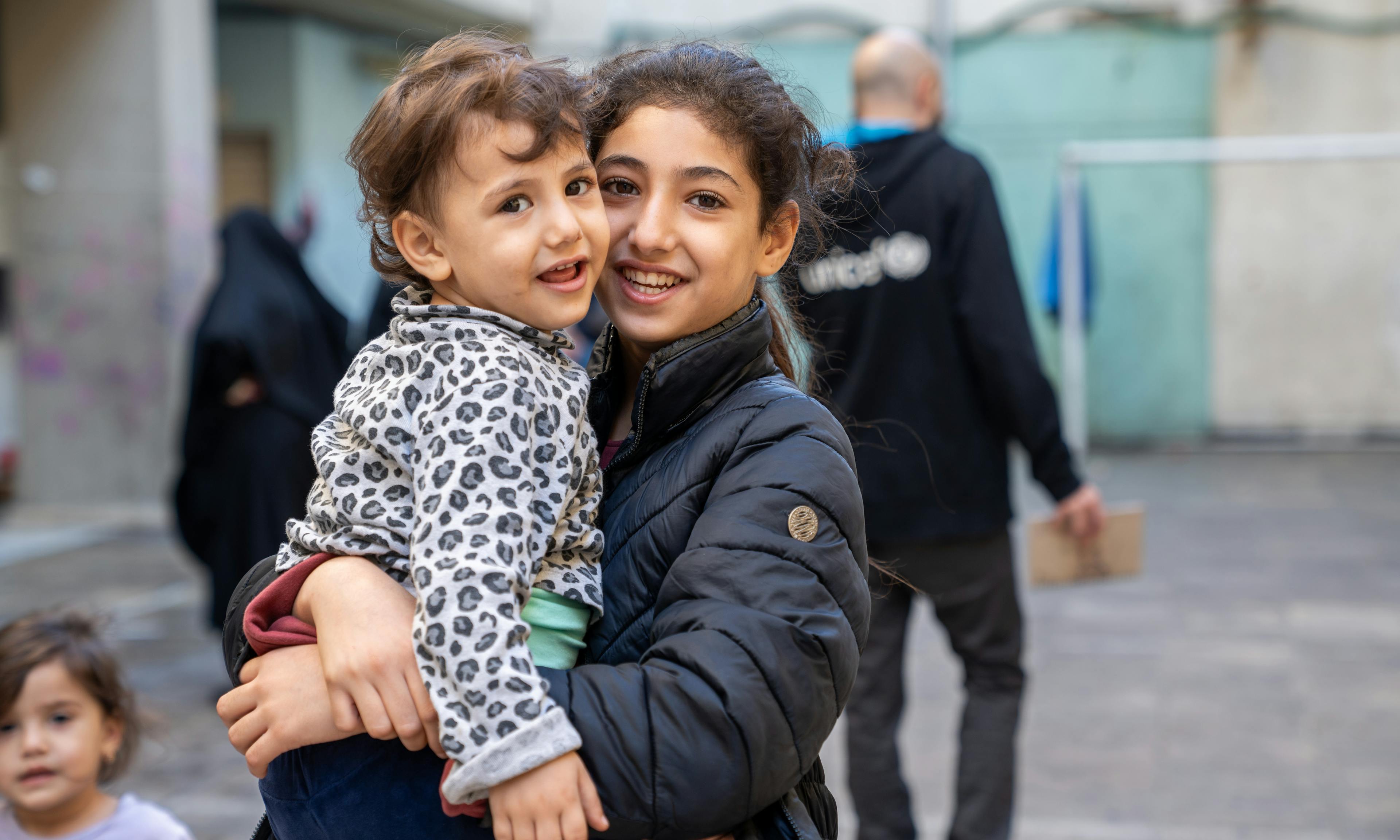 Hawraa, 3 years old with her sister Zeinab, 11 years old. In a school turned shelter, children play in the hallways, finding brief moments of normalcy despite the war in Lebanon.