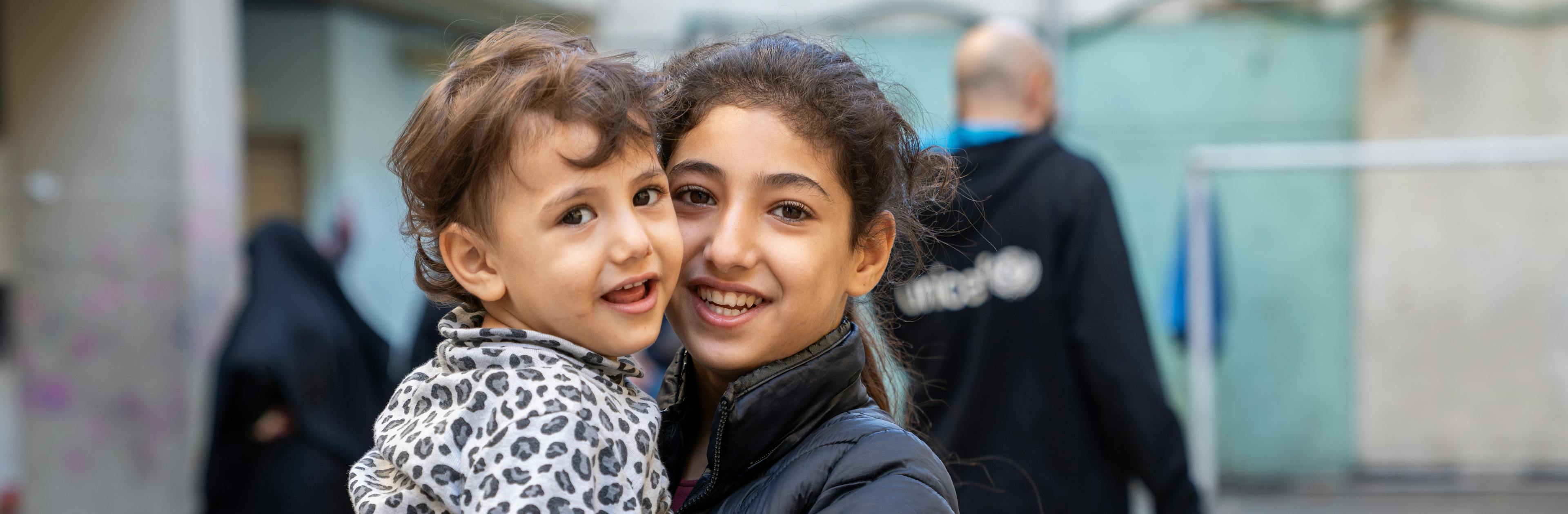 Hawraa, 3 years old with her sister Zeinab, 11 years old. In a school turned shelter, children play in the hallways, finding brief moments of normalcy despite the war in Lebanon.