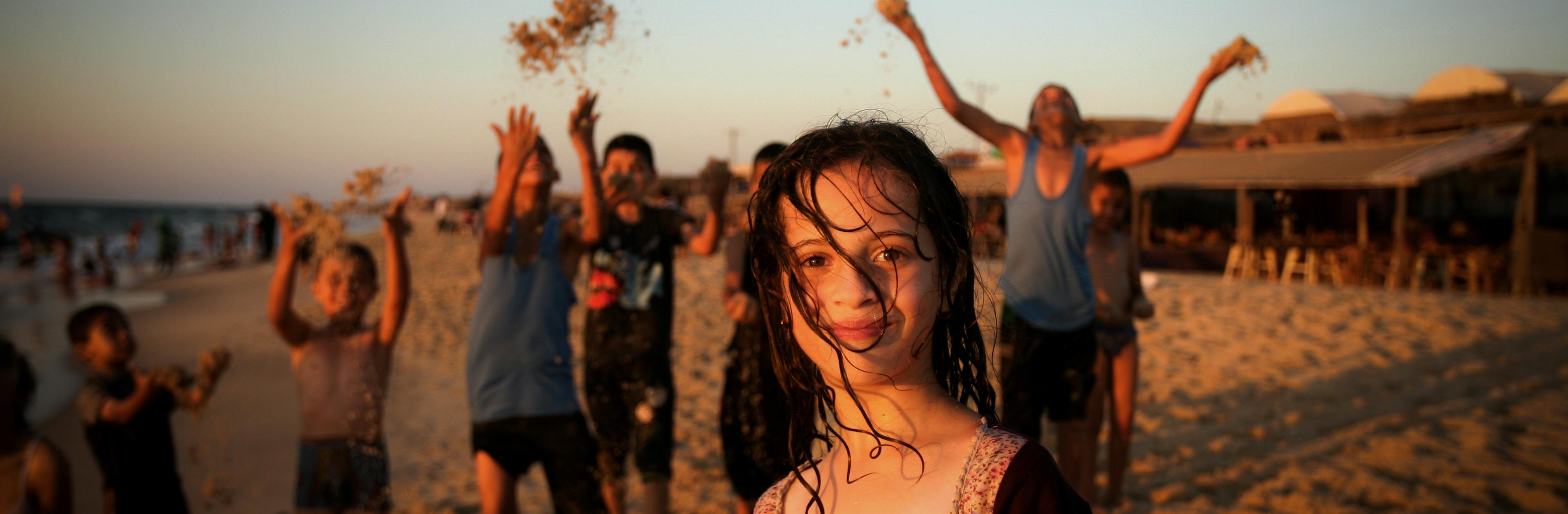 Kids on the beach throwing sand in the air.