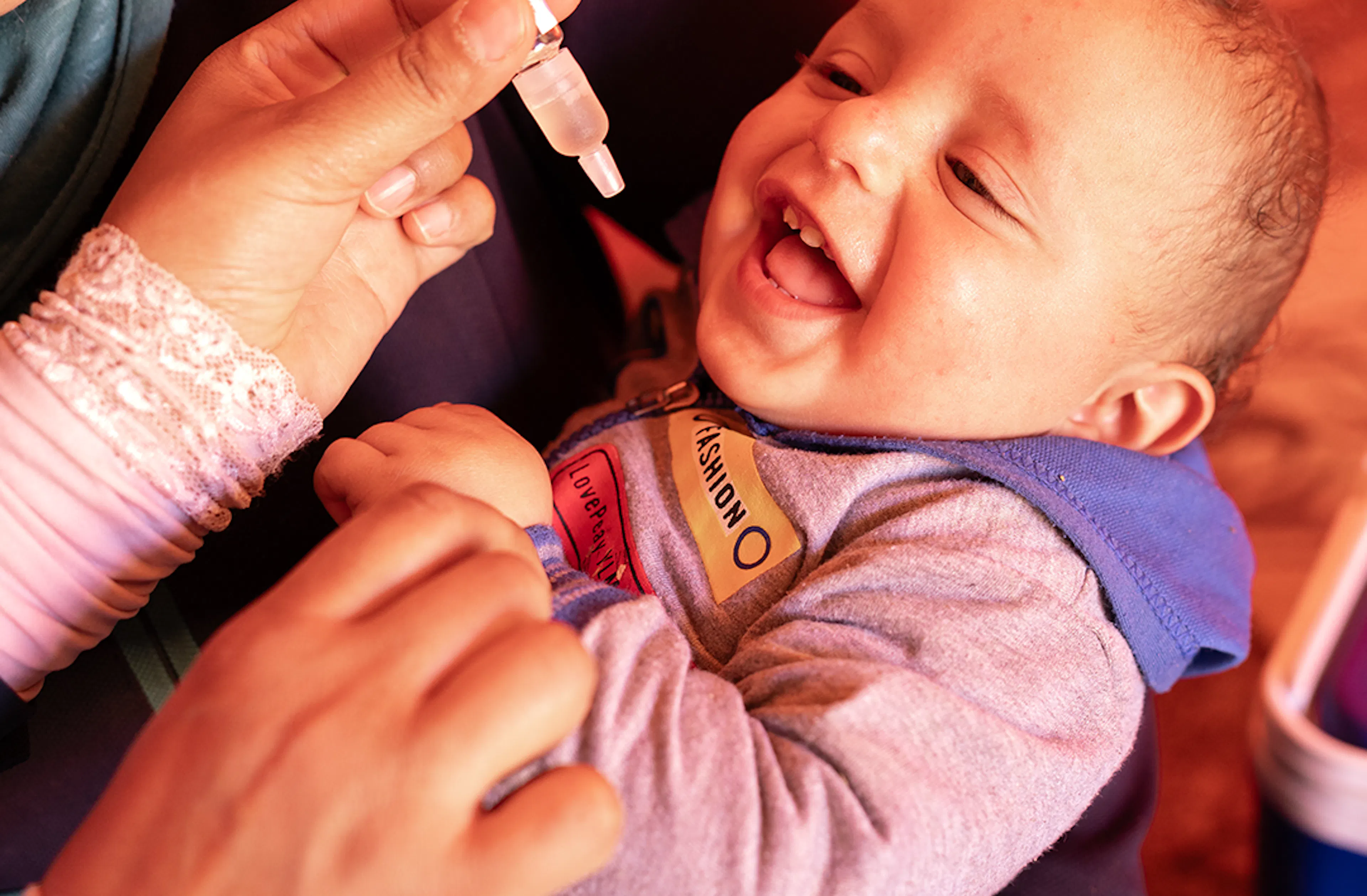 Ameer, 11 months, receives his MMR vaccine and an OPV vaccine from health worker Amal in an informal tented settlement in Ajloun. The vaccination occurs during a mobile immunization team visit to this hard-to-reach community, supported by UNICEF.