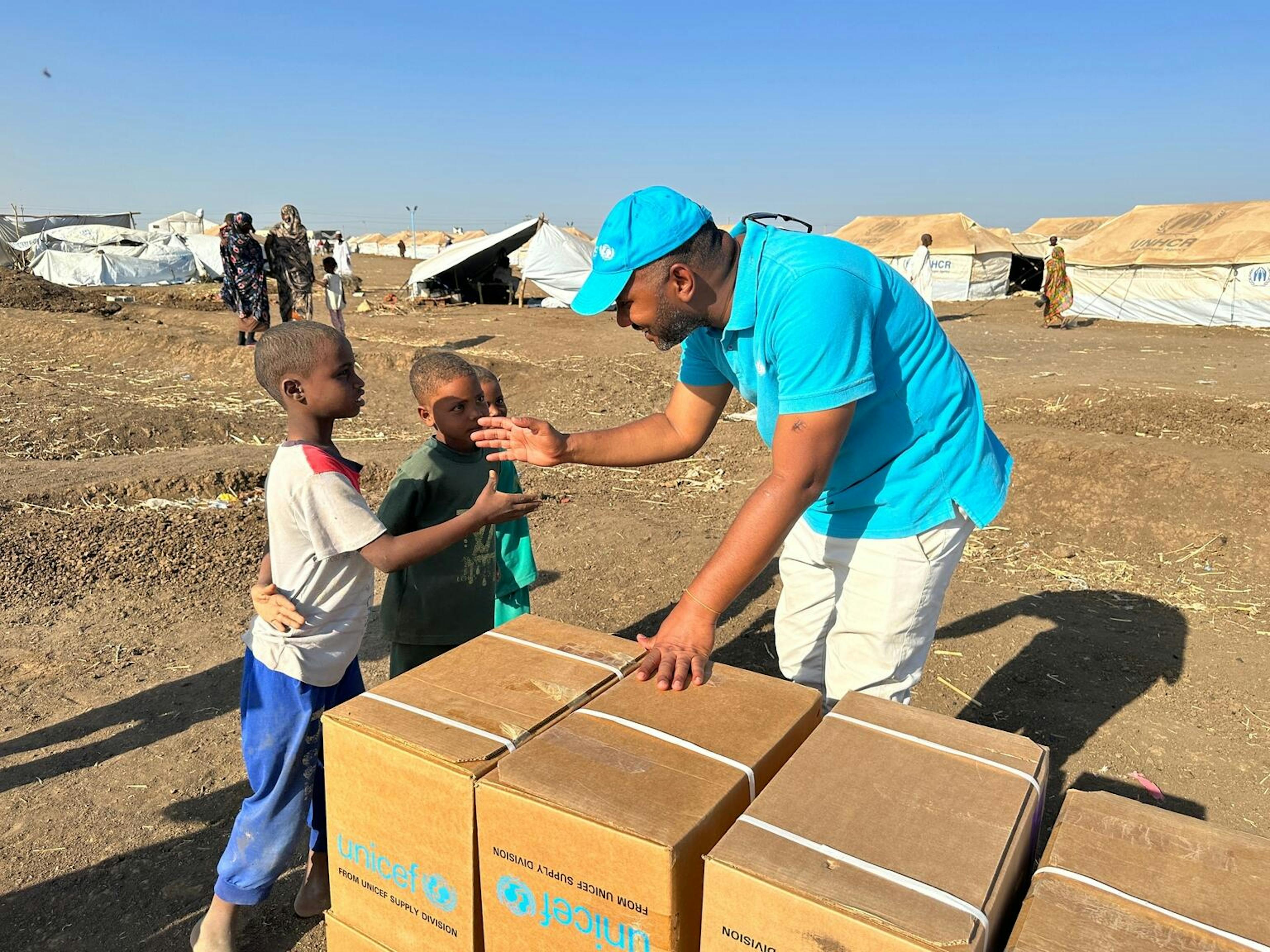 UNICEF aid worked wearing blue uniform shaking hands with Sudan child