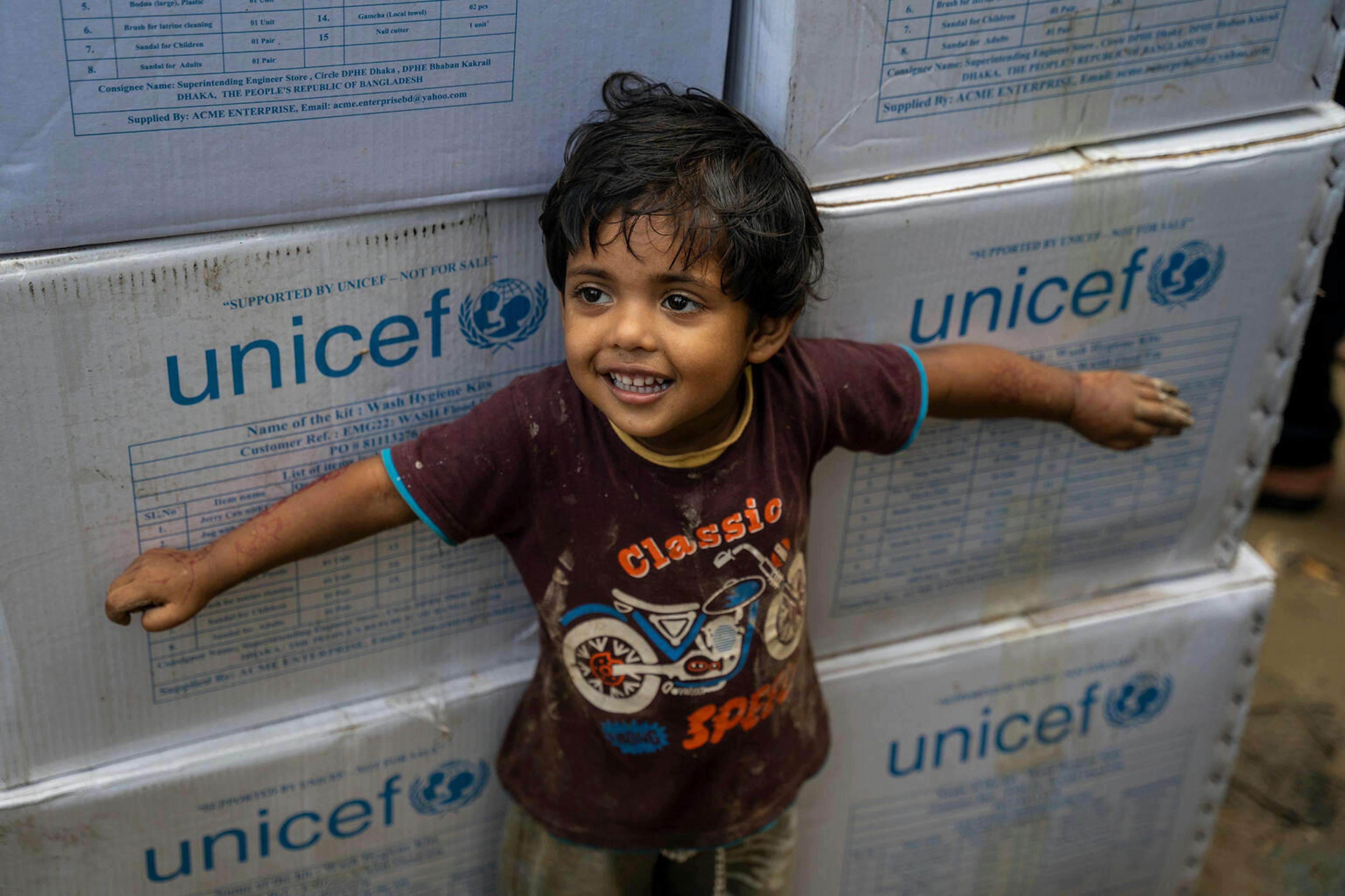 Child stands in front of emergency supplies sent by UNICEF in the aftermath of flooding in Bangladesh