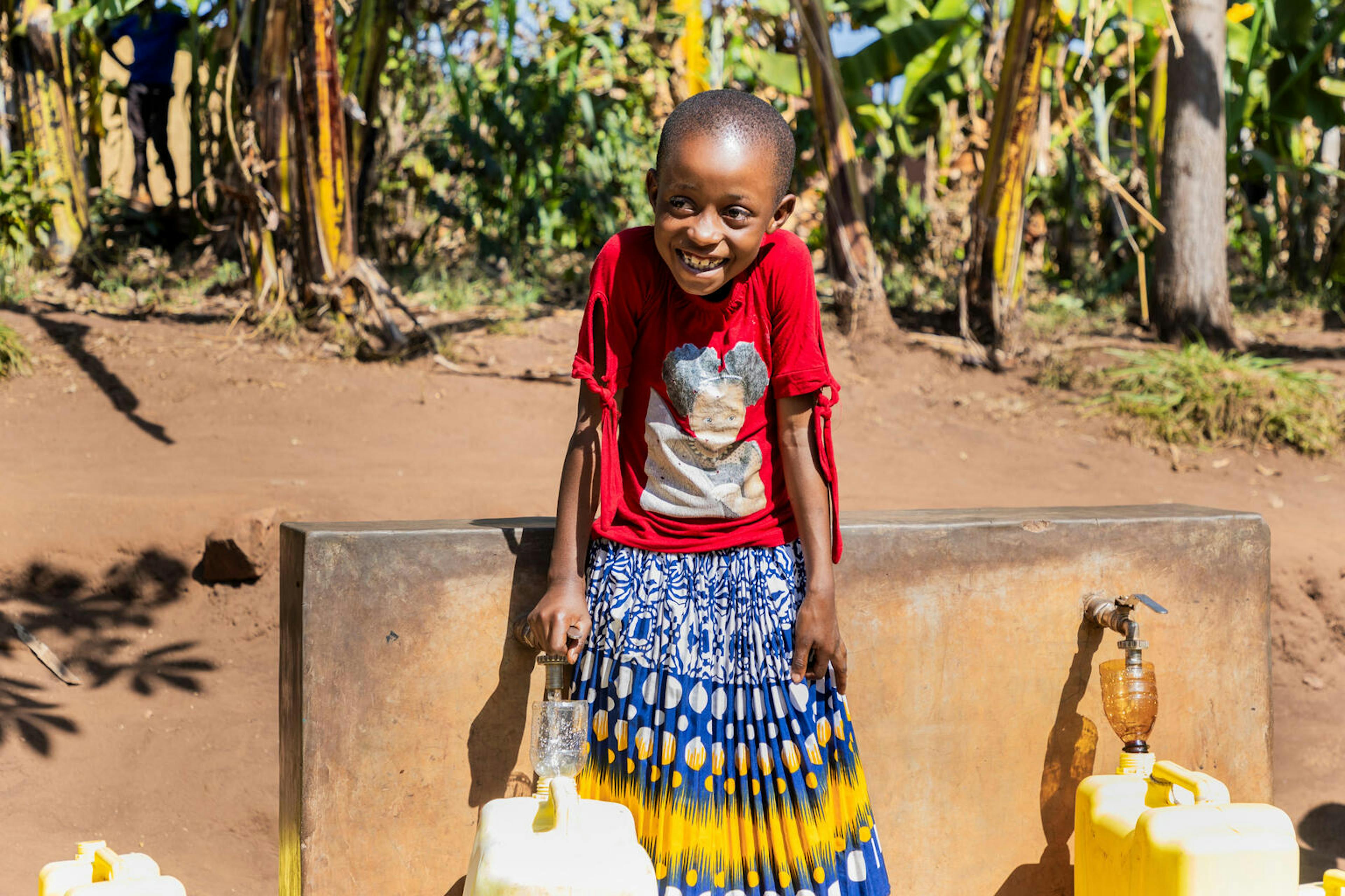 8-year-old Bonette fills water containers from taps that are part of a solar-powered water supply system in her neighbourhood in Kigarama Sector, Kirehe District, Eastern Province of Rwanda.
