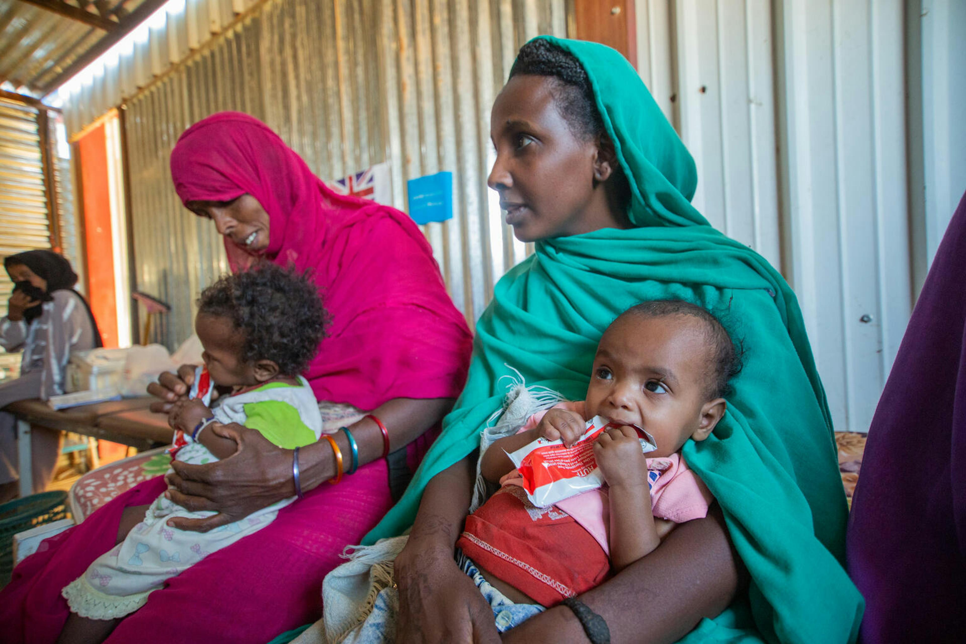 Malaz (right) carries her two-year-old Aida as she eats ready-to-use-therapeutic food at Al-Arab health facility, Kassala State.