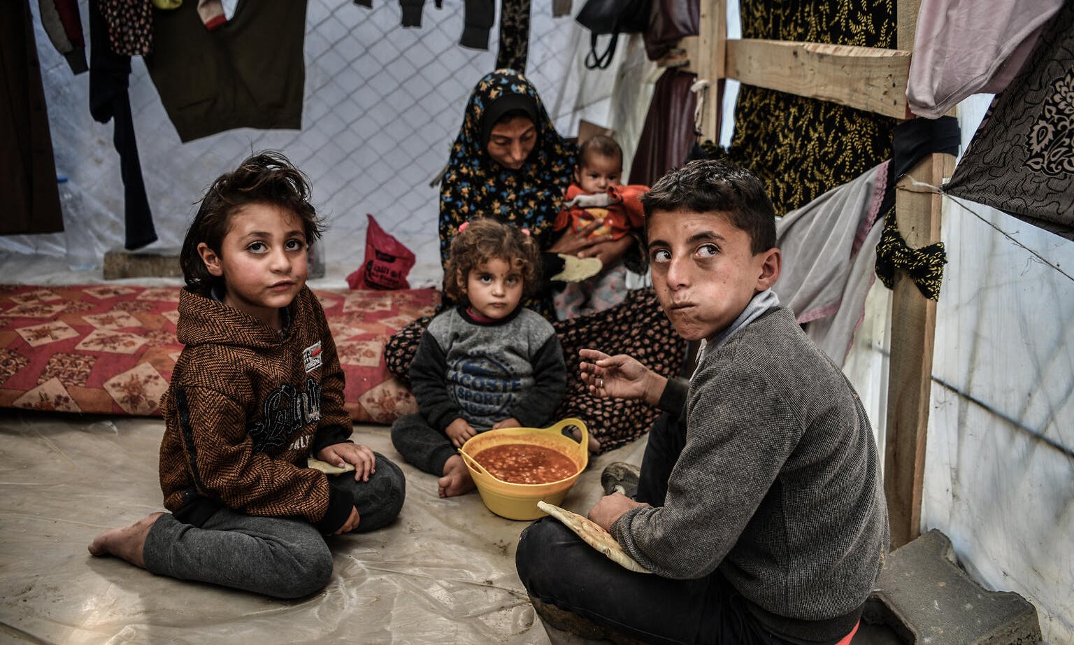 Muhammad (11) with his mother and three sisters sharing a bowl of beans in their tent in Rafah, Gaza.