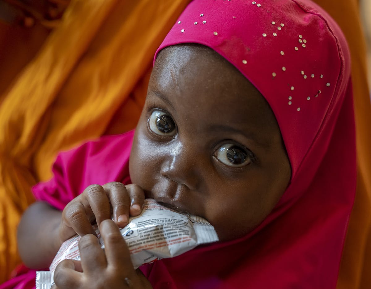 2-year-old Luul Hassan sits on the lap of her mother, 30-year-old Salaado Kerow, and eats from a sachet of ready-to-use therapeutic food (RUTF) after being assessed for malnutrition at the outpatient therapeutic centre (OTP) in the Alla Futo camp for internally displaced people on the outskirts of Mogadishu.