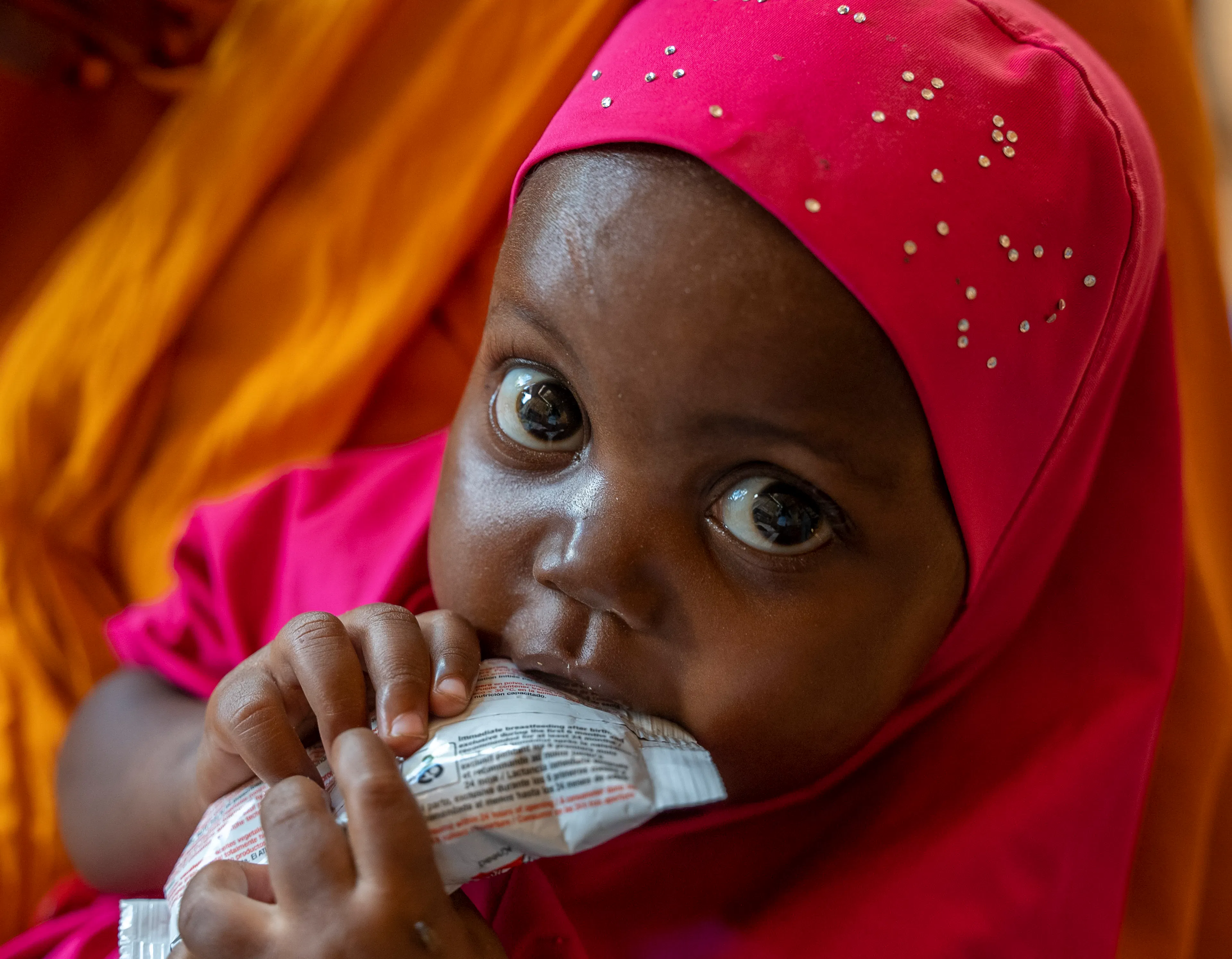 2-year-old Luul Hassan sits on the lap of her mother, 30-year-old Salaado Kerow, and eats from a sachet of ready-to-use therapeutic food (RUTF) after being assessed for malnutrition at the outpatient therapeutic centre (OTP) in the Alla Futo camp for internally displaced people on the outskirts of Mogadishu.
