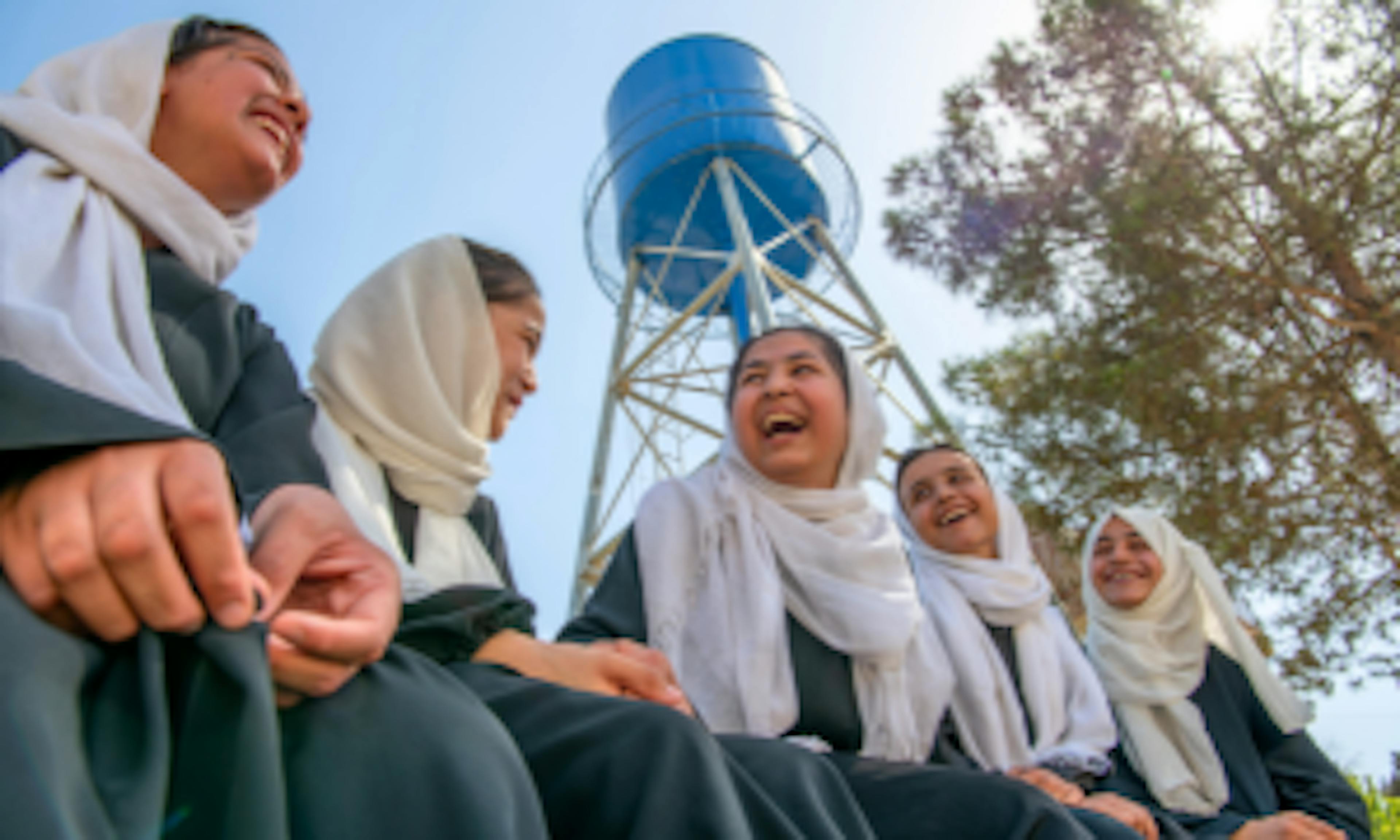 A group of students talk and laugh near the UNICEF-installed water tank.