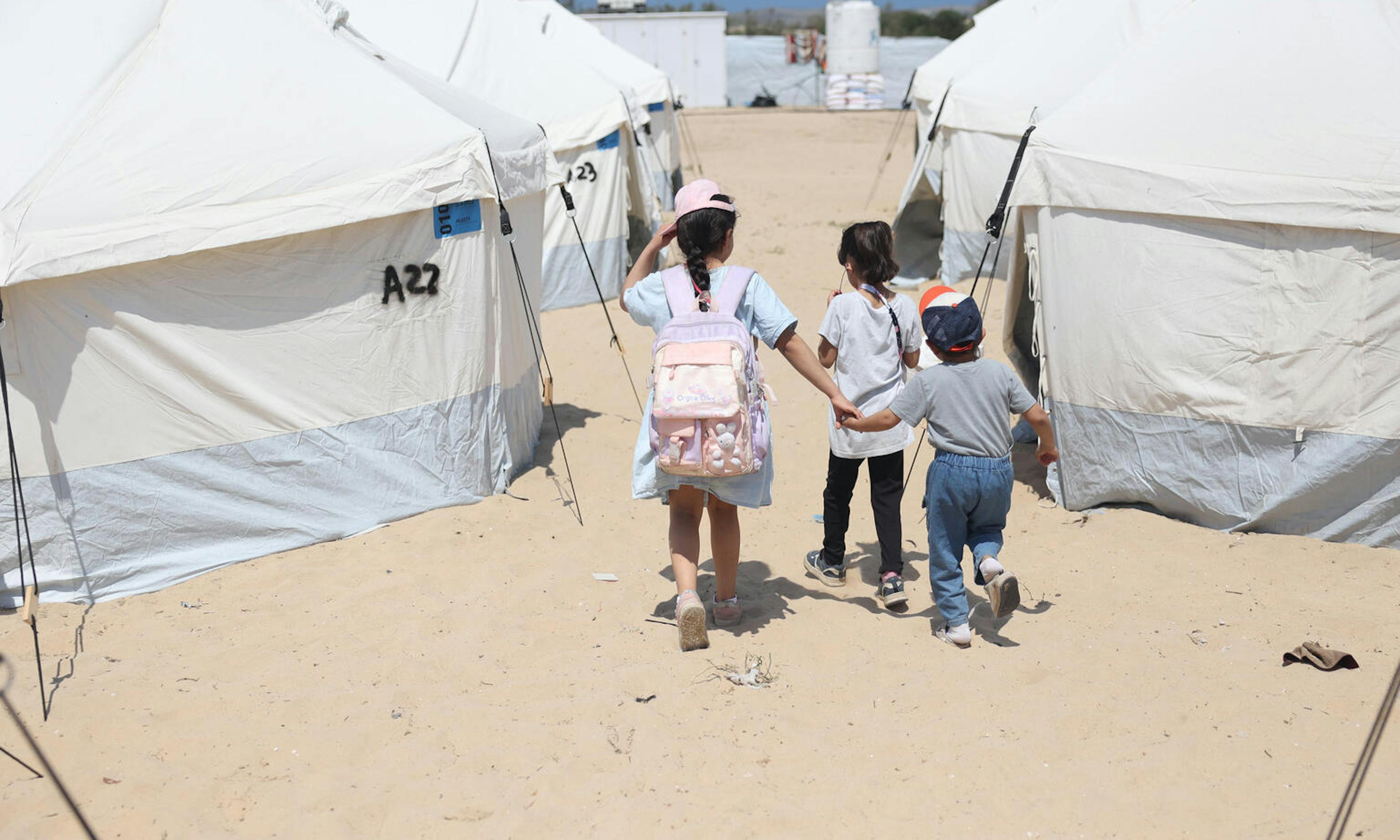 children walking hand in hand through a camp in Rafah