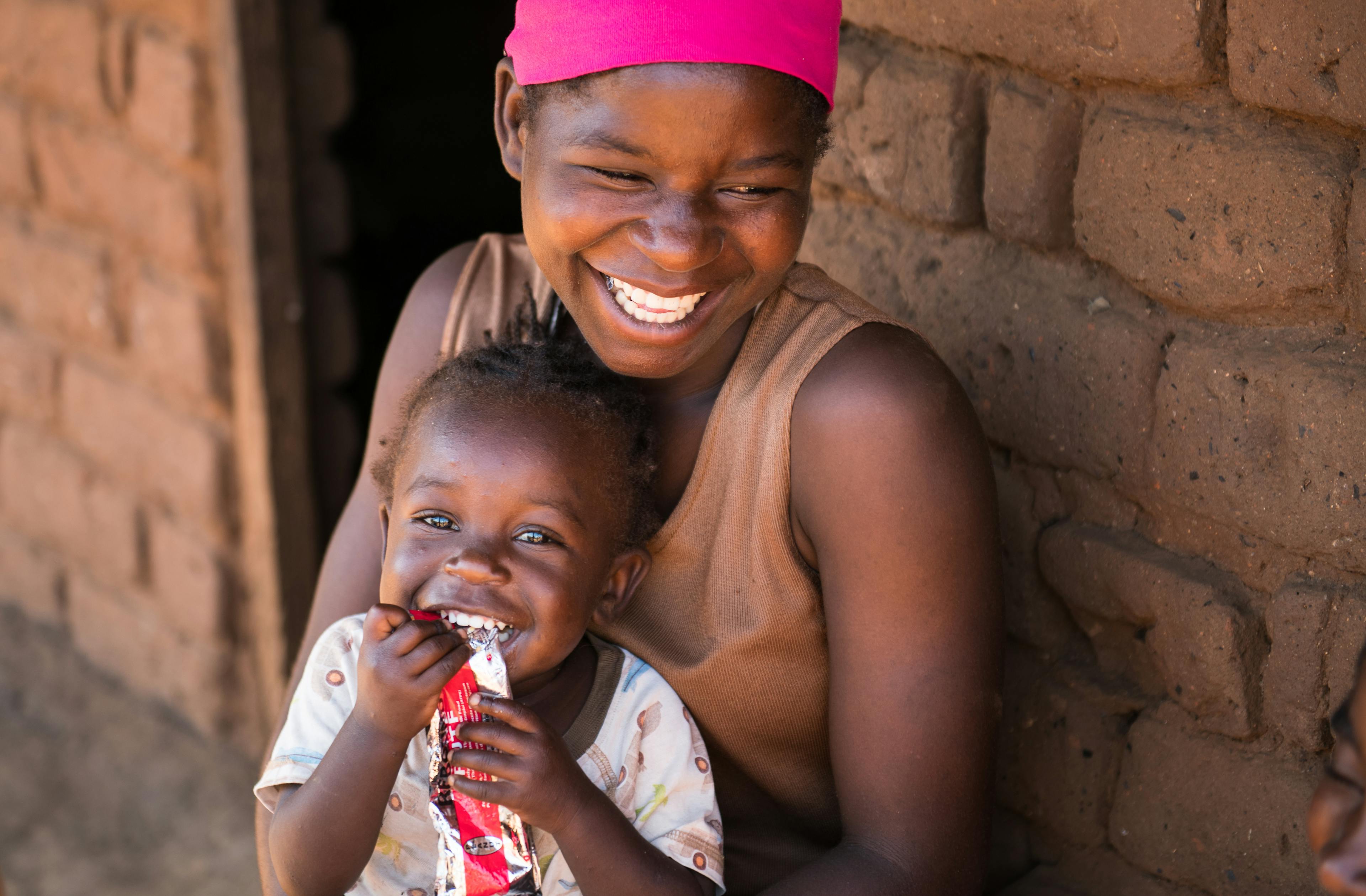 20-year-old Edna Maunde smiles as her daughter, 2-year-old Christina Cosmas as she eats RUTF at their home in Mavila Village, southern Malawi.