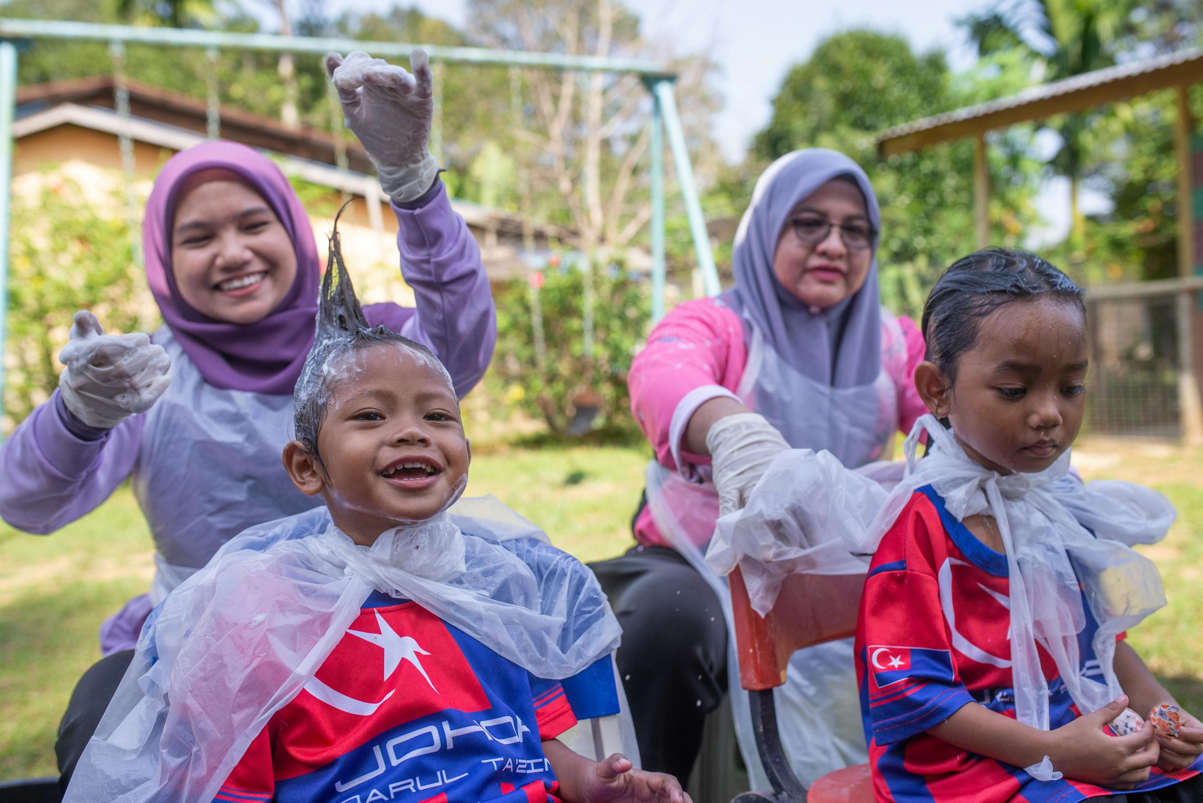 Amelin Deliana (5) and Tantiana Robel (5) receive a hair care session during a mobile health clinic program organized by the Mersing District Health Office at their kindergarten.