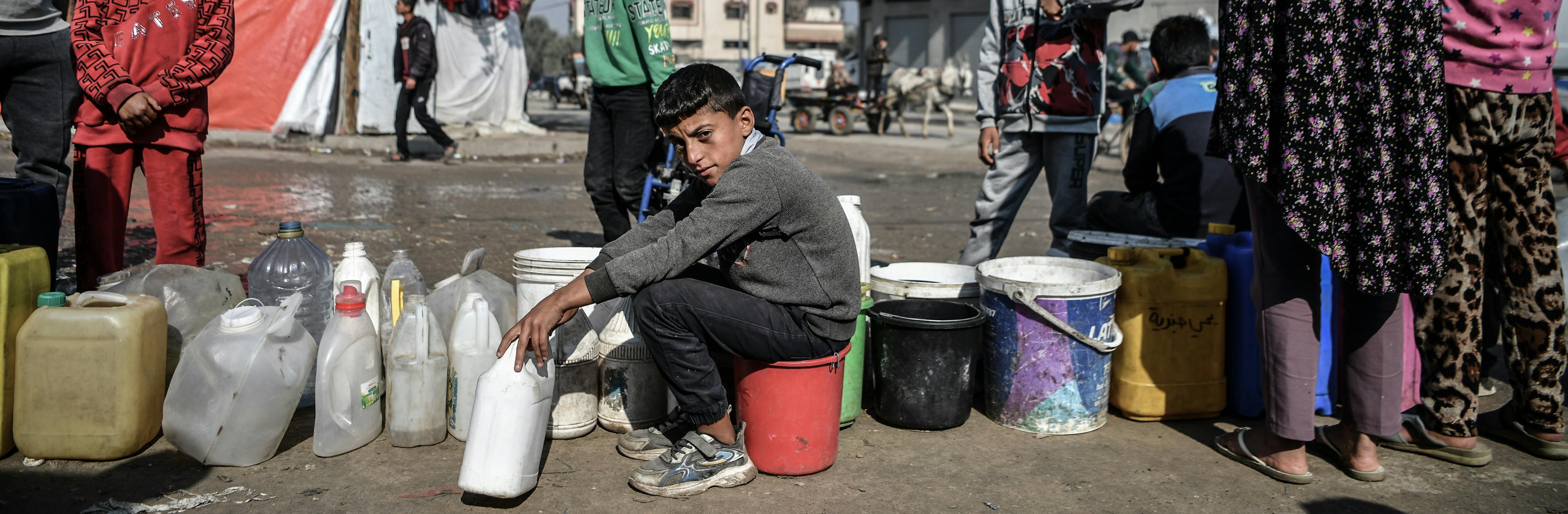 Muhammad, 11-year-old, in line between gallons of water, waiting his turn to fill clean drinking water for his family that was displaced to Rafah, south of the Gaza Strip because of the ongoing war.