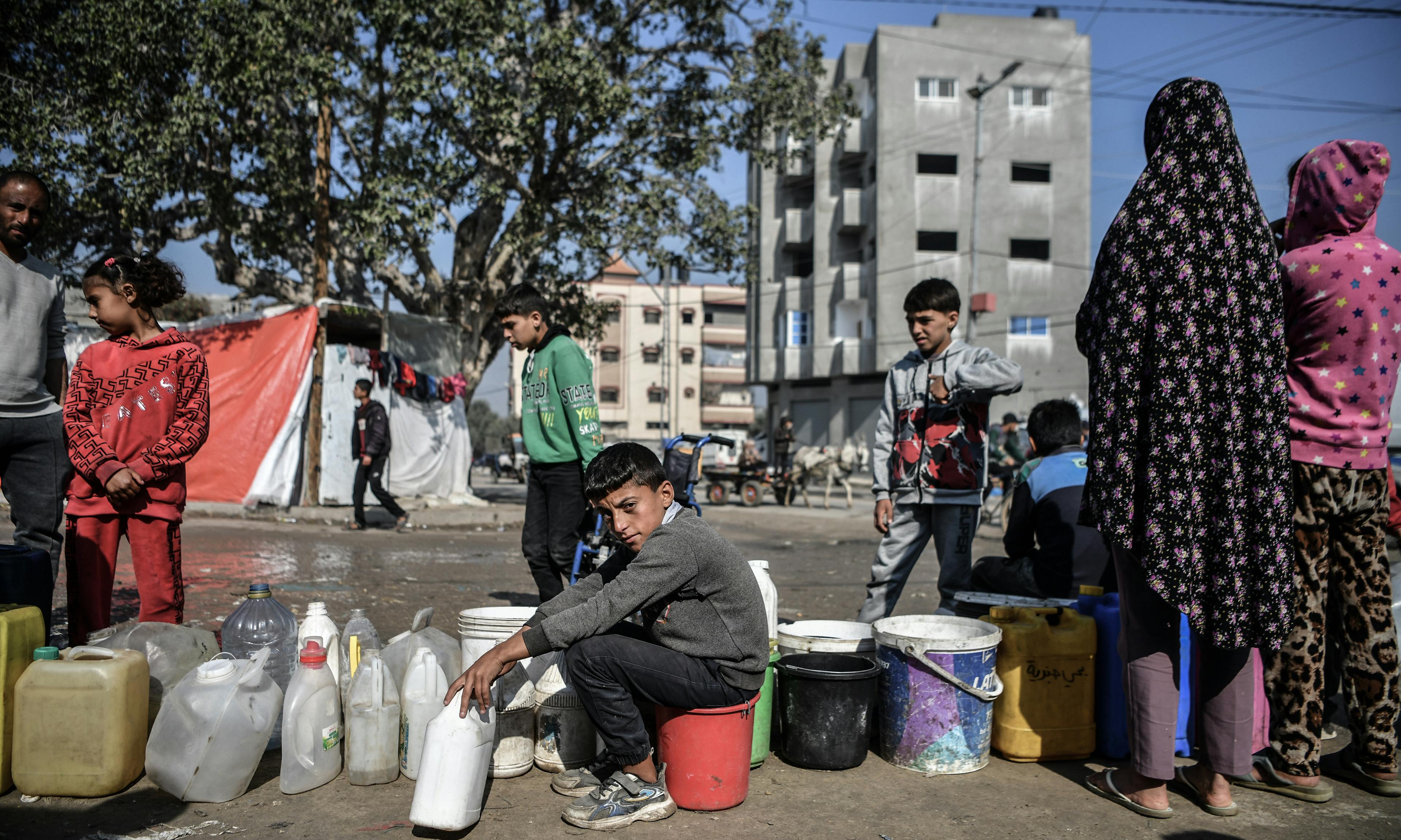 Muhammad, 11-year-old, in line between gallons of water, waiting his turn to fill clean drinking water for his family that was displaced to Rafah, south of the Gaza Strip because of the ongoing war.

