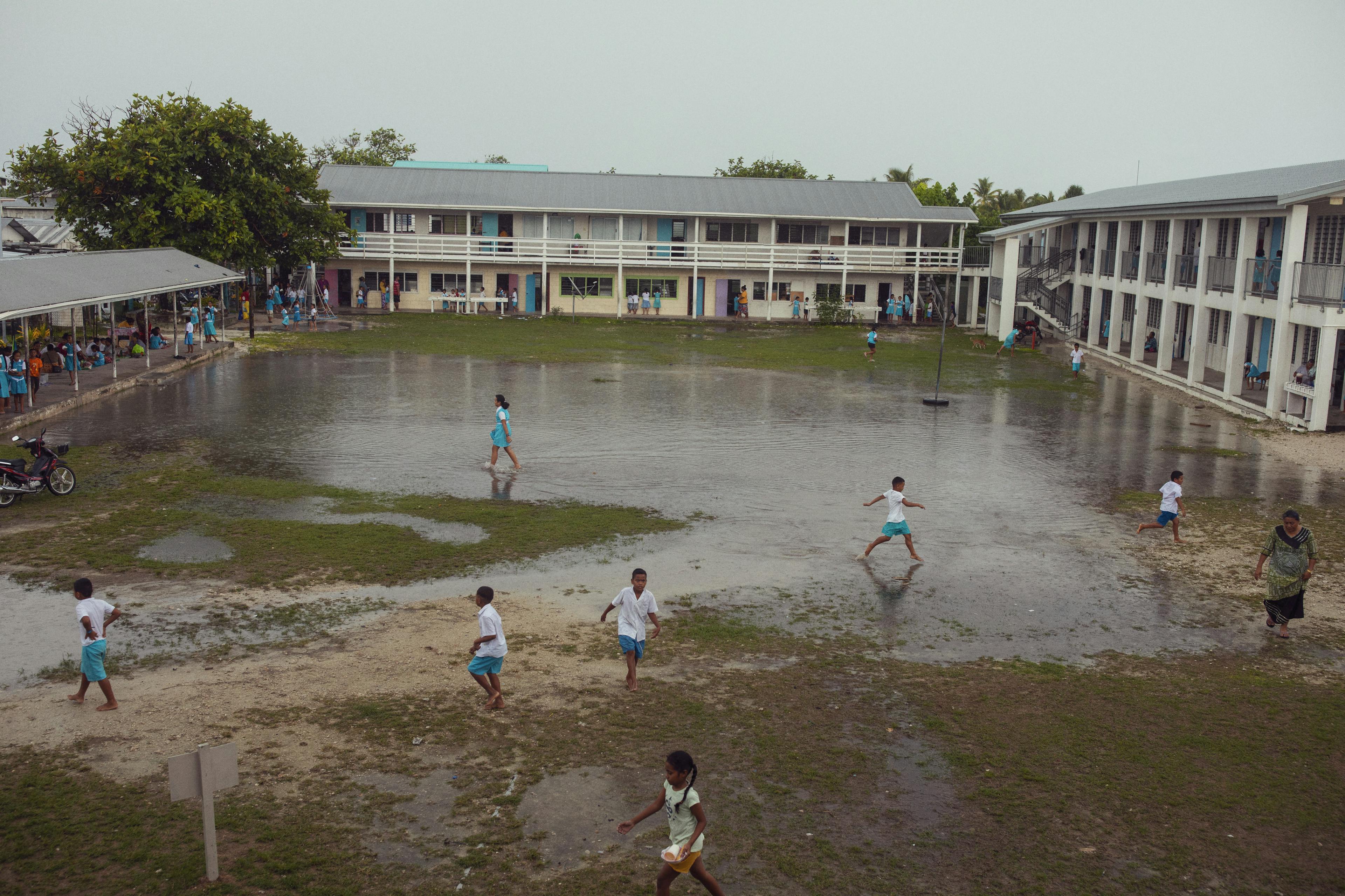 Students of the largest school in Tuvalu, Nauti Primary, wade through their flooded schoolyard.