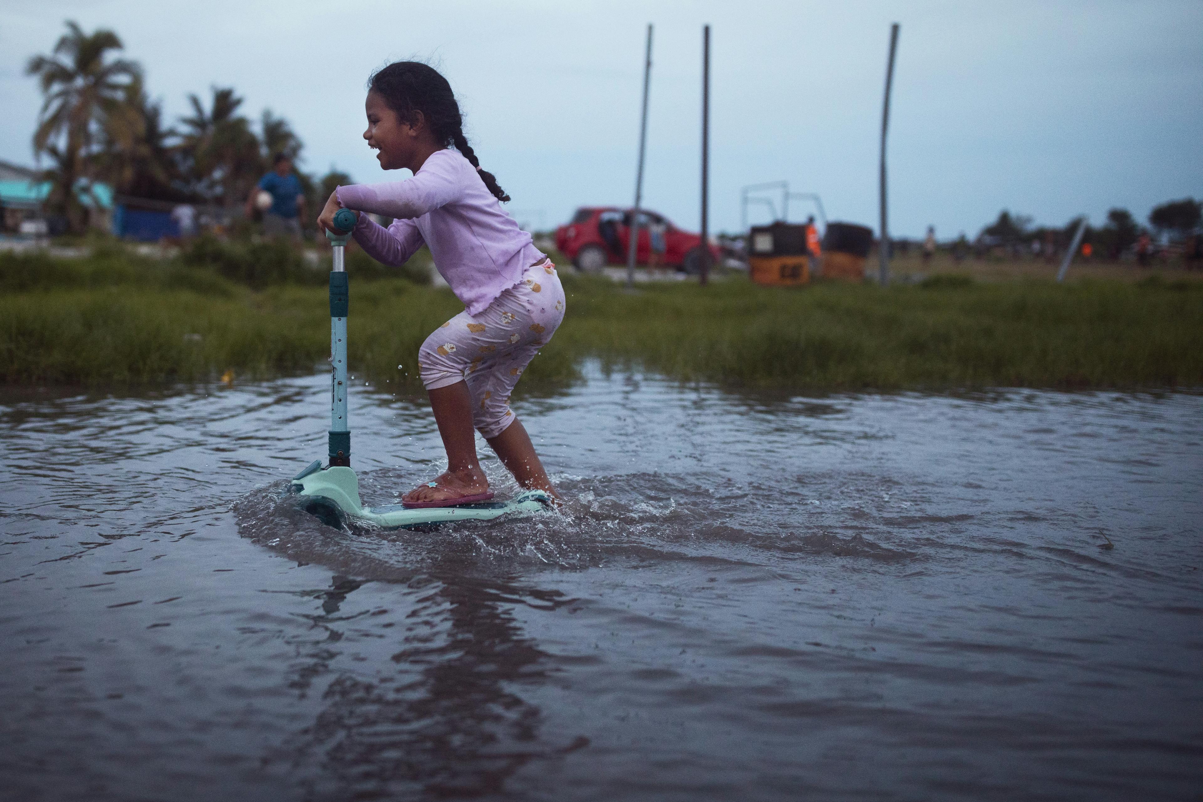 A small child pushing her scooter through flooded terrain in Tuvalu.