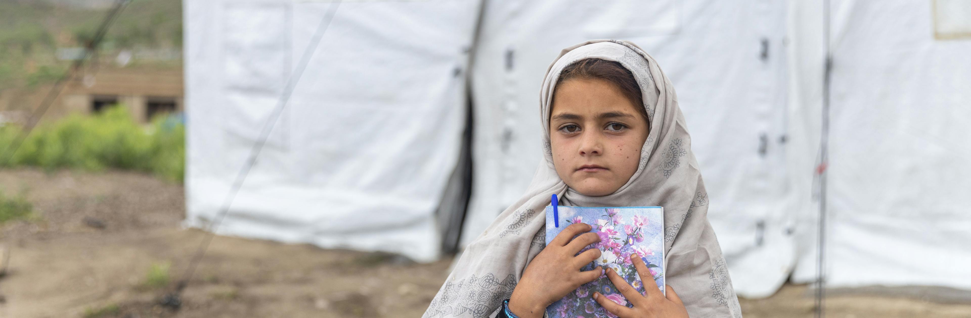 A little girl clutches her notebook outside a UNICEF-supported child-friendly space in Gayan District, Paktika Province, Afghanistan. This child-friendly space was established in the community to help children cope with their trauma after the June 2022 earthquake.