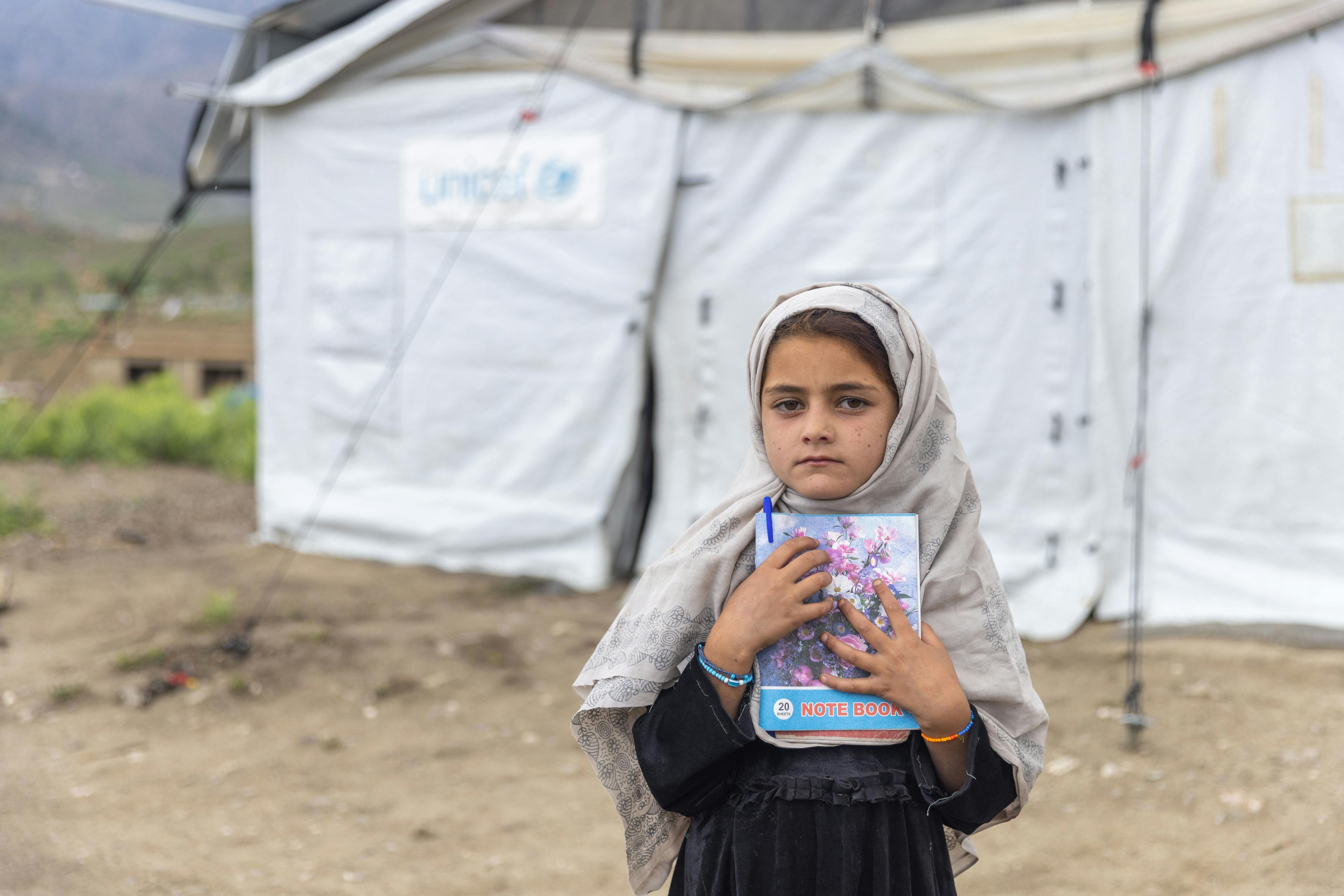 A little girl clutches her notebook outside a UNICEF-supported child-friendly space in Gayan District, Paktika Province, Afghanistan. This child-friendly space was established in the community to help children cope with their trauma after the June 2022 earthquake.