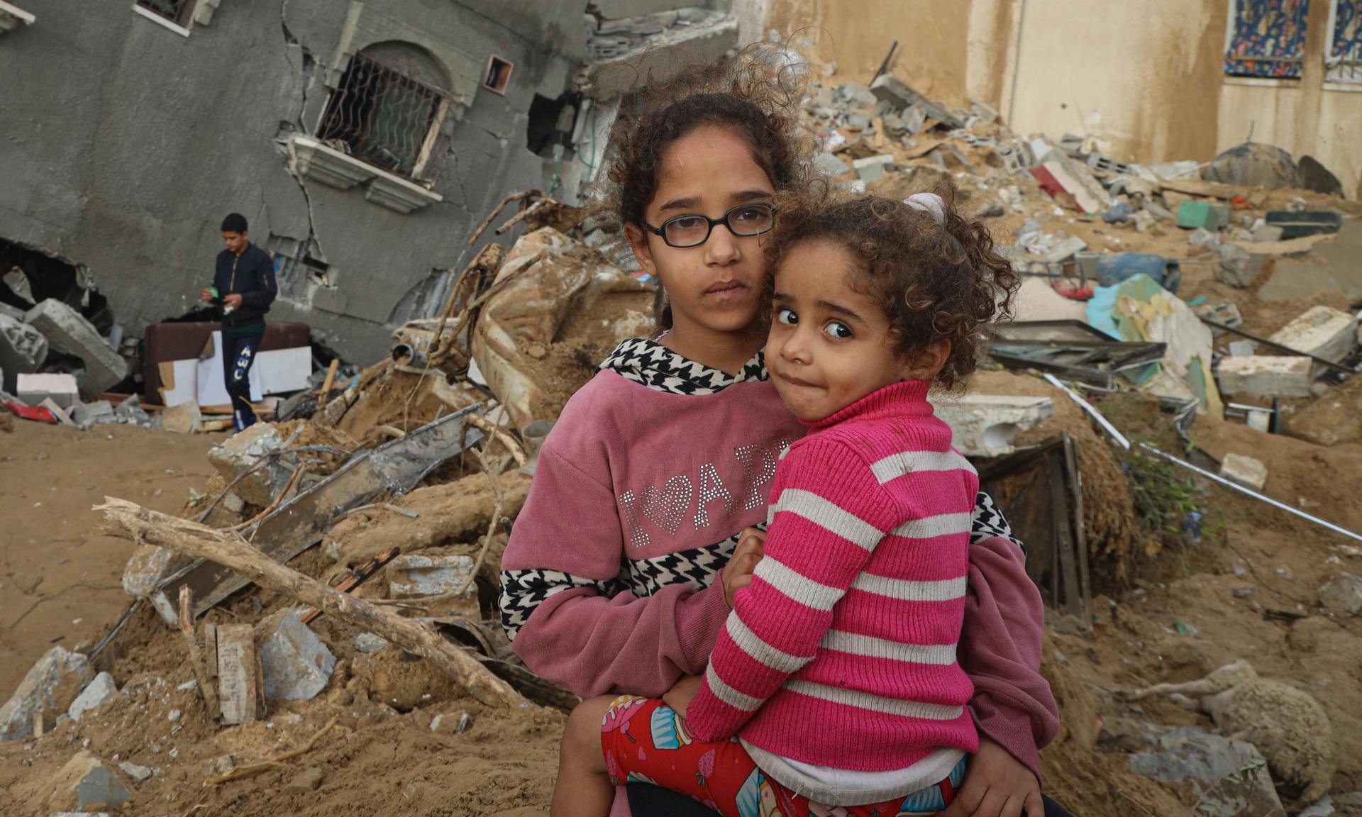 Abeer (12) and Zahra (4) stand in front of their destroyed house. The sisters are two of the more than 1.5 million kids in need of humanitarian assistance in Gaza.