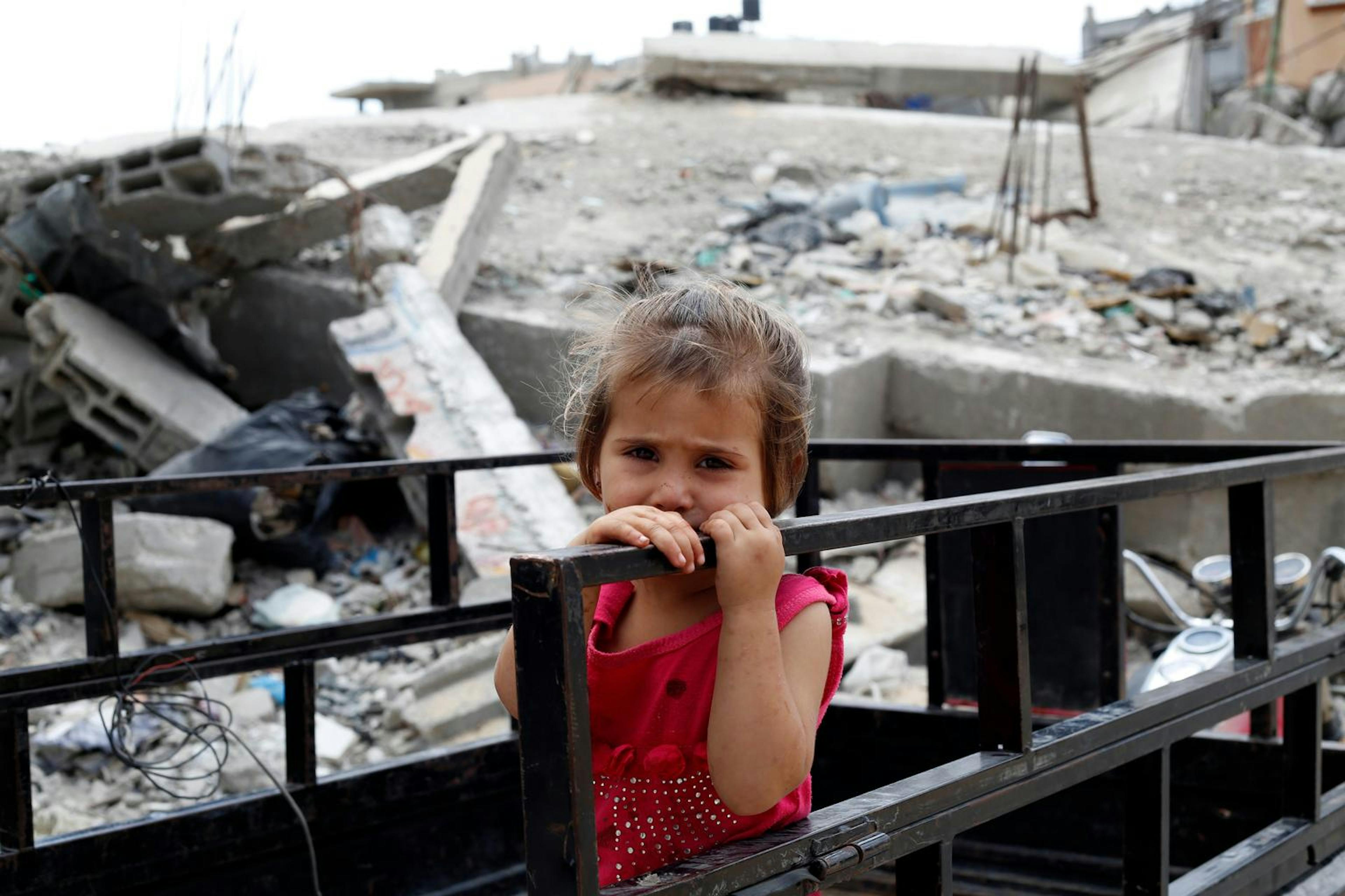 A young girl holds a railing outside her family’s partially destroyed home in Gaza City