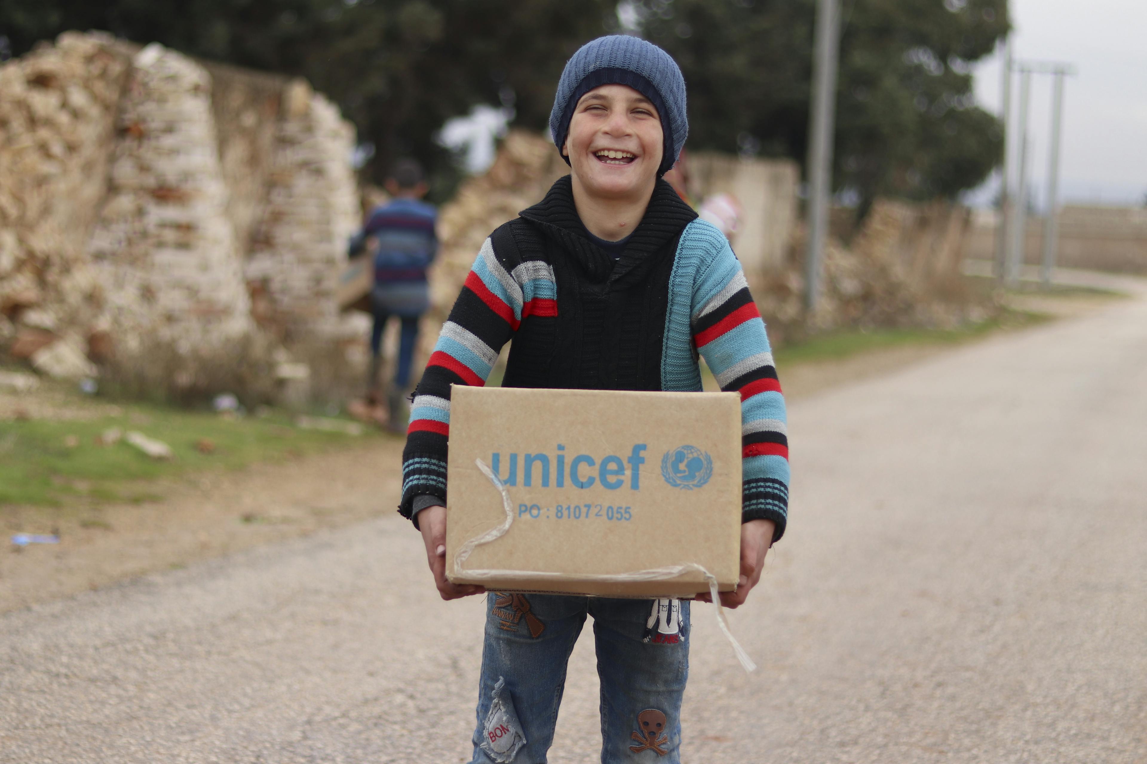 9-year-old Ibrahim, carries his newly received winter clothing kit. Aleppo, Syria.