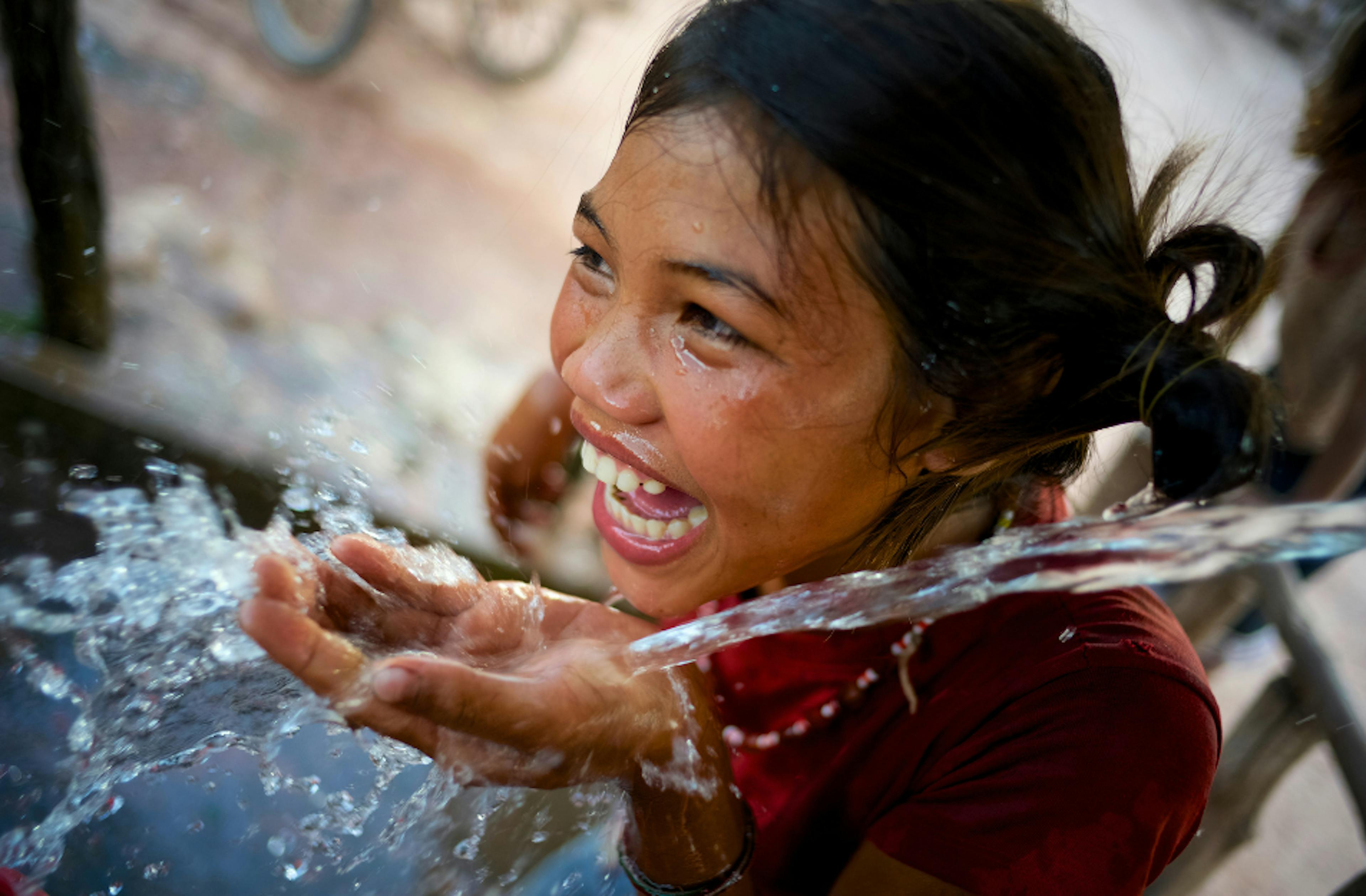 A girl laughs playfully while drinking water at a water point in Adone village, Laos.