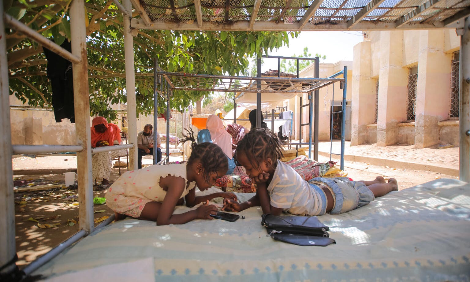Displaced children play games on a mobile phone at a temporary shelter, following continued fighting that broke out in Khartoum on 15 April. Children and their families have fled and sought safety in neighbouring safer states.