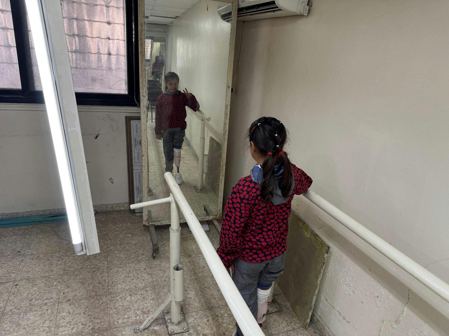 8-year-old Ritaj stands in front of a mirror. Her leg was amputated due to maggot infestation