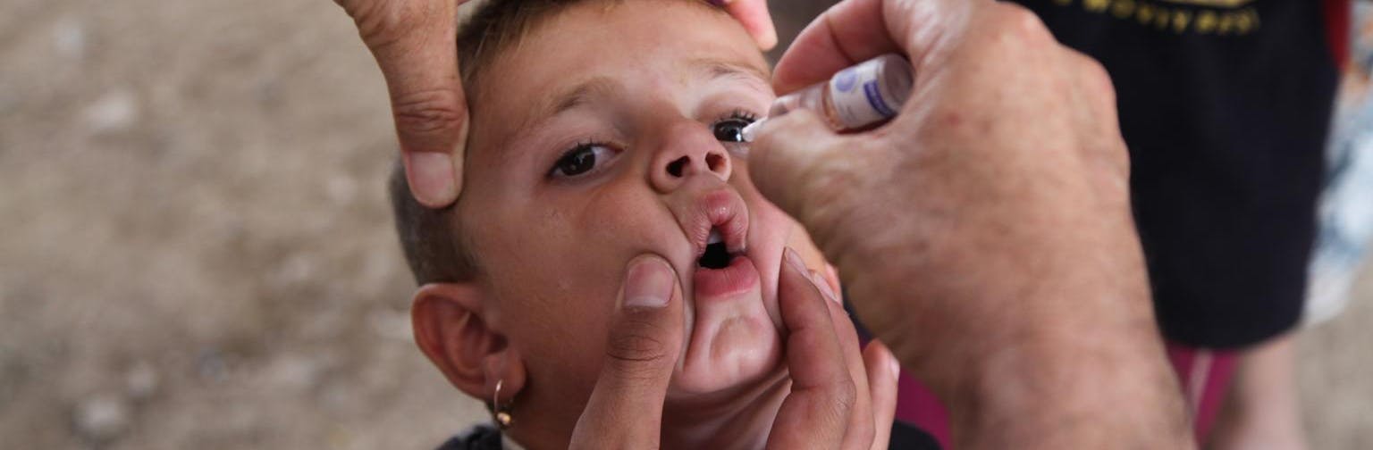 A health worker gives a dose of oral polio vaccine to a boy in Iraq.
