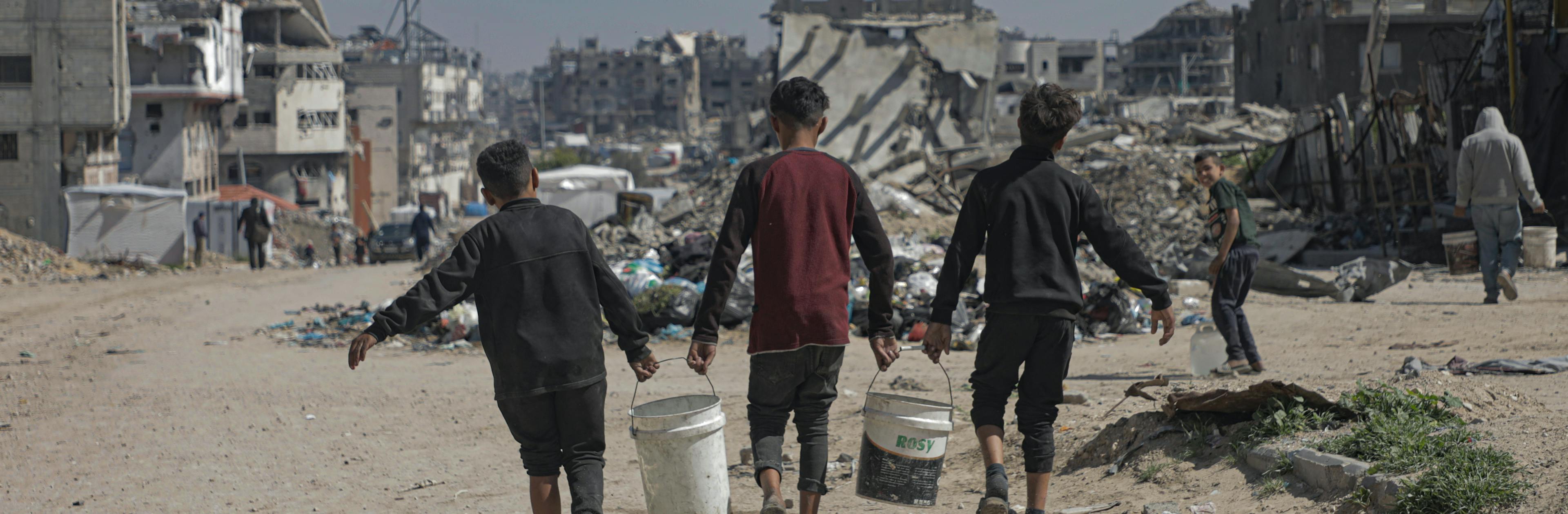 On 24 March 2025 in the State of Palestine, children carry water containers back to their tents in Beach Camp, Gaza City, after filling them from tanks of safe water brought by UNICEF trucks.
