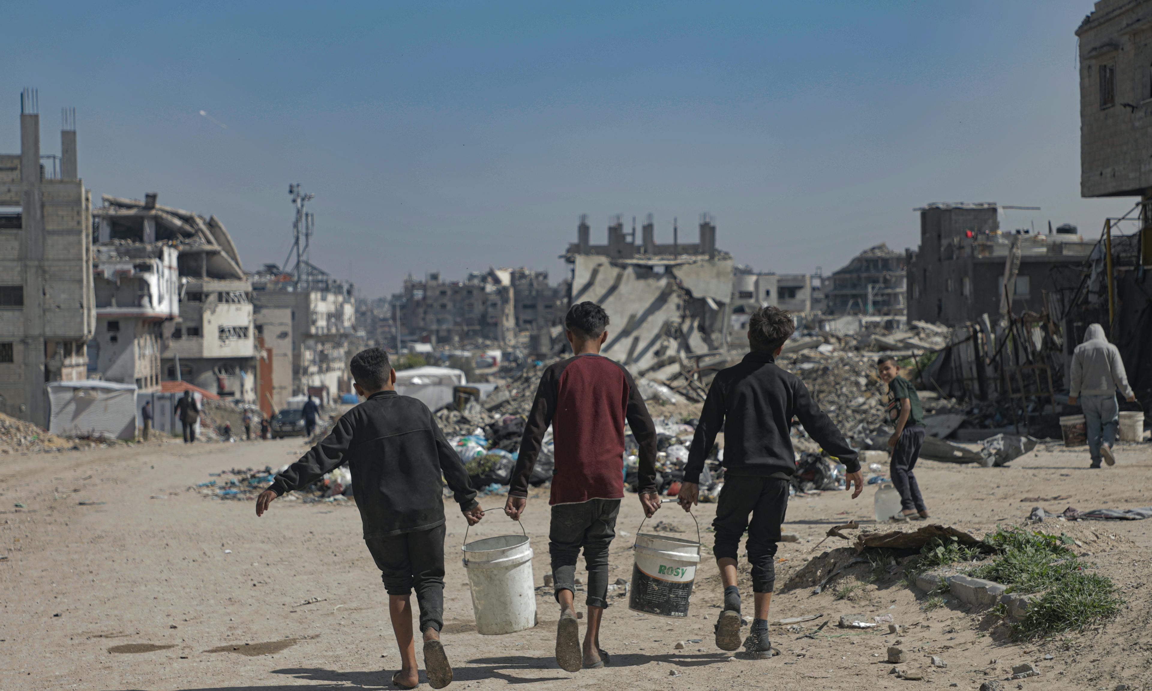 On 24 March 2025 in the State of Palestine, children carry water containers back to their tents in Beach Camp, Gaza City, after filling them from tanks of safe water brought by UNICEF trucks.

