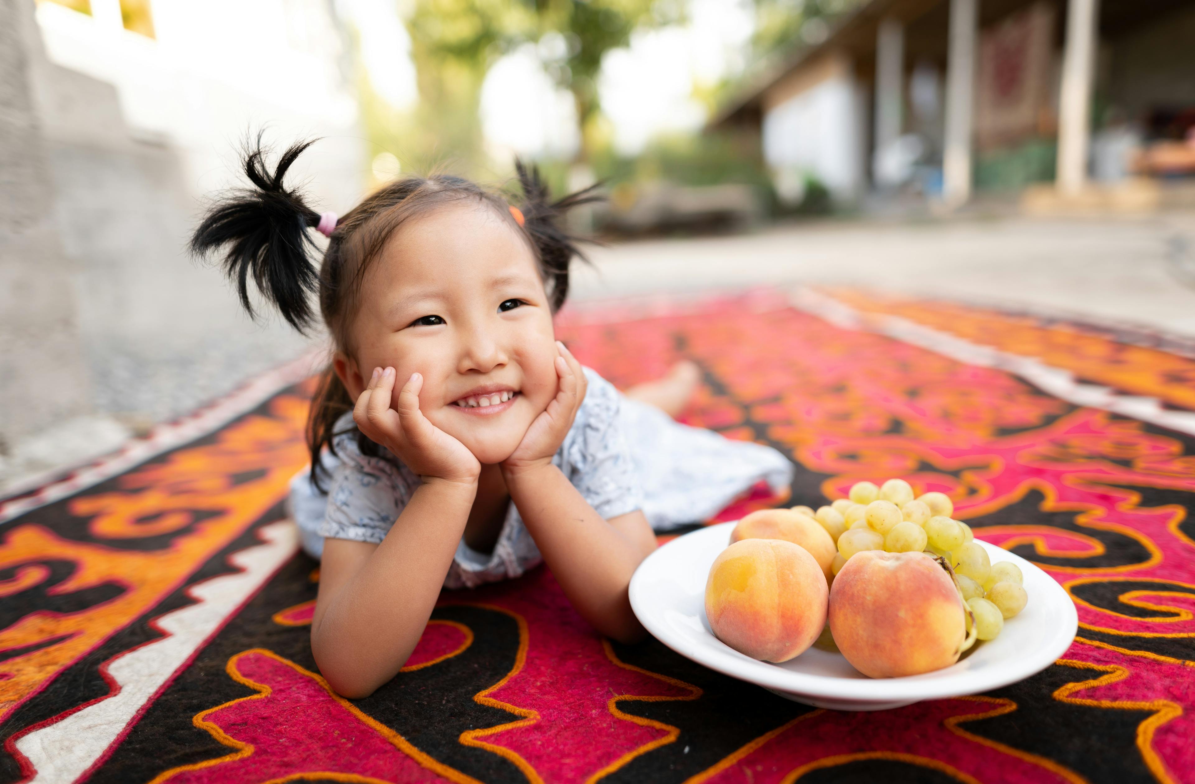 Nurayim, 3 years old, poses for a photo with a plate of fruit at her home in Kurshab village, Uzgen district, Osh Oblast, Kyrgyzstan. Her mother tells us that she adapted well to eating food that the rest of the family eats – dairy products, meat fish, poultry, eggs, fruits and vegetables. The family avoids unhealthy foods in every way possible.