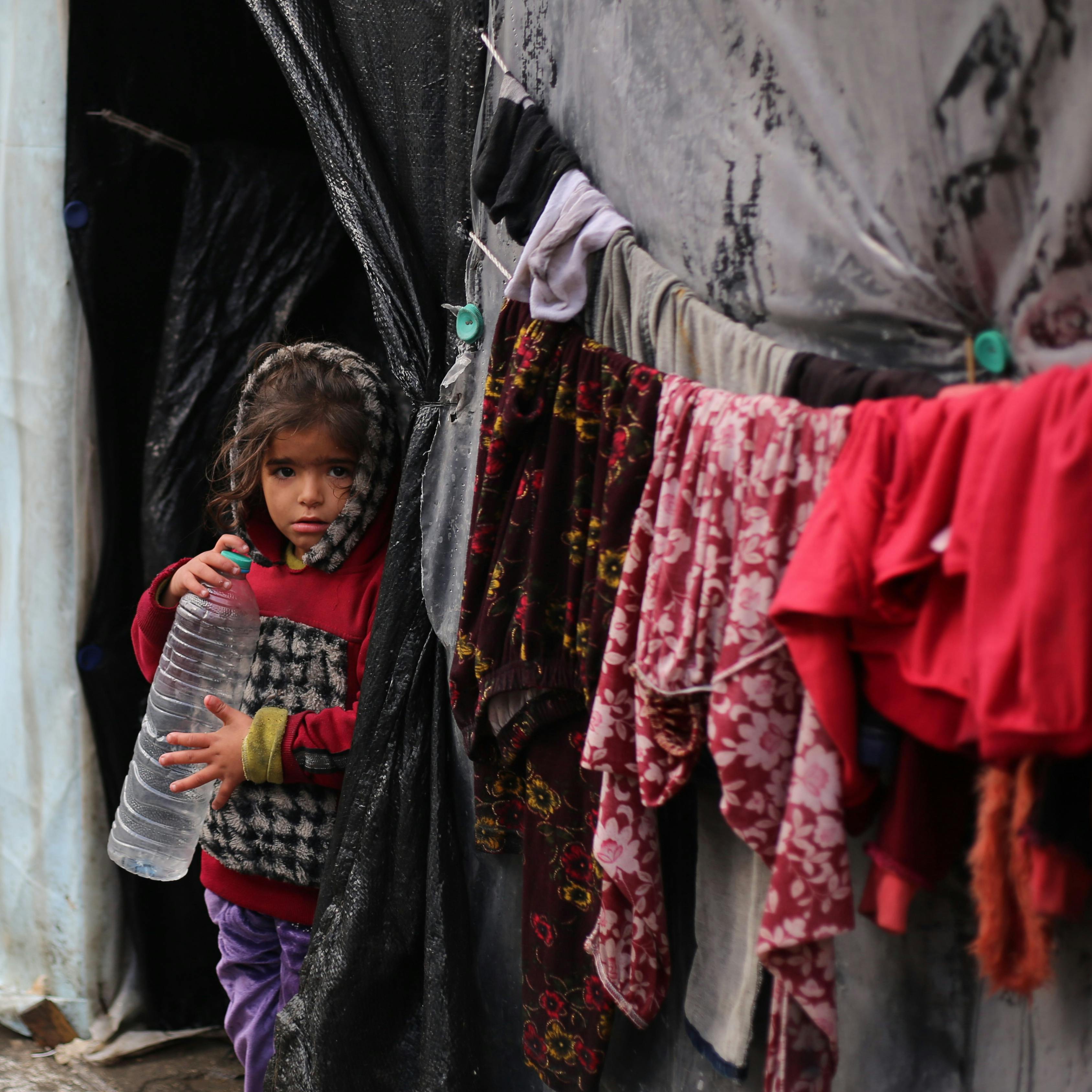 In a rainy day, a girl stands in front of her in the city of Rafah, south of the Gaza Strip, while holding an empty water bottle.