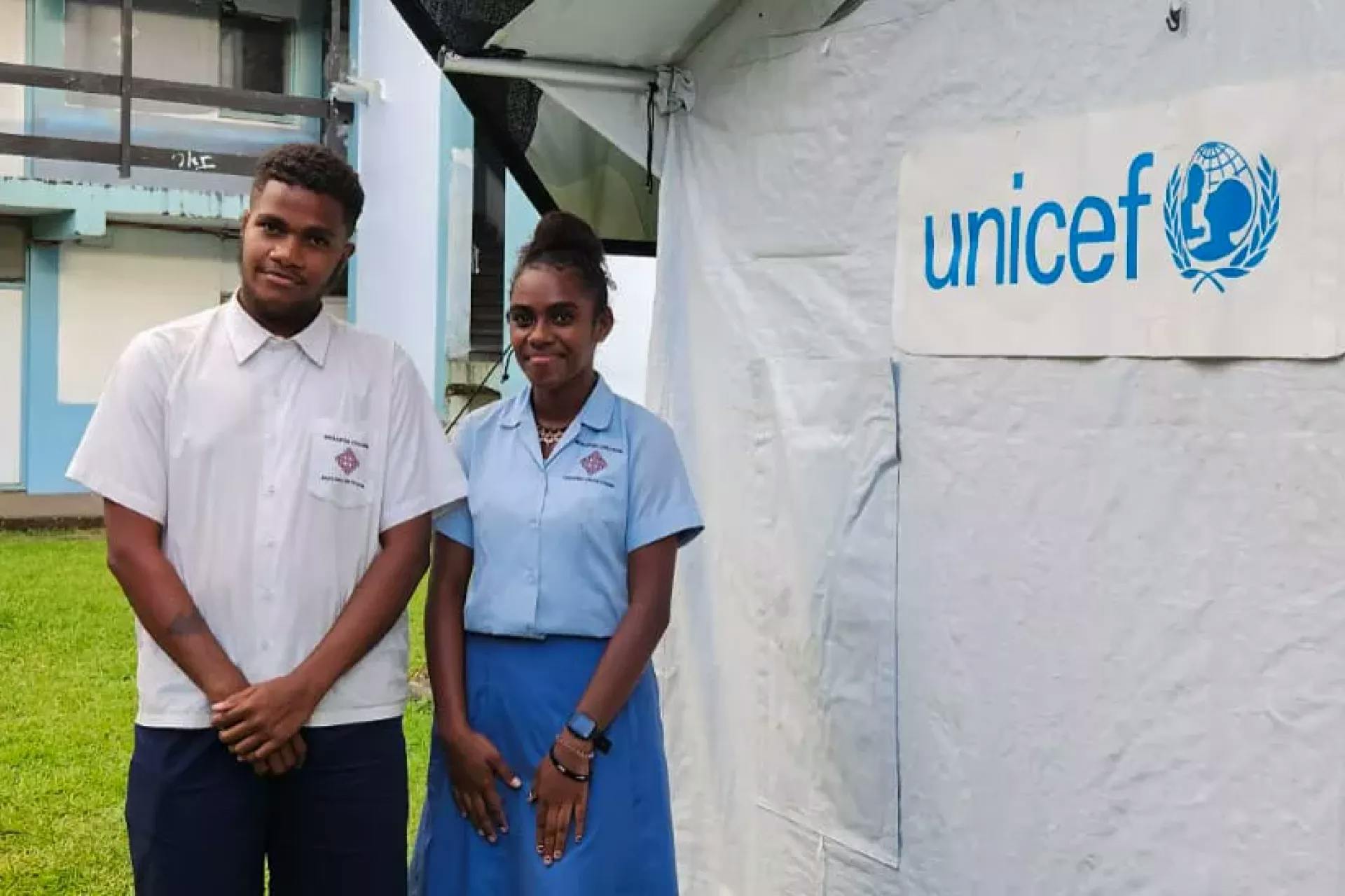 Two teenagers in Vanuatu stand by a UNICEF sign.