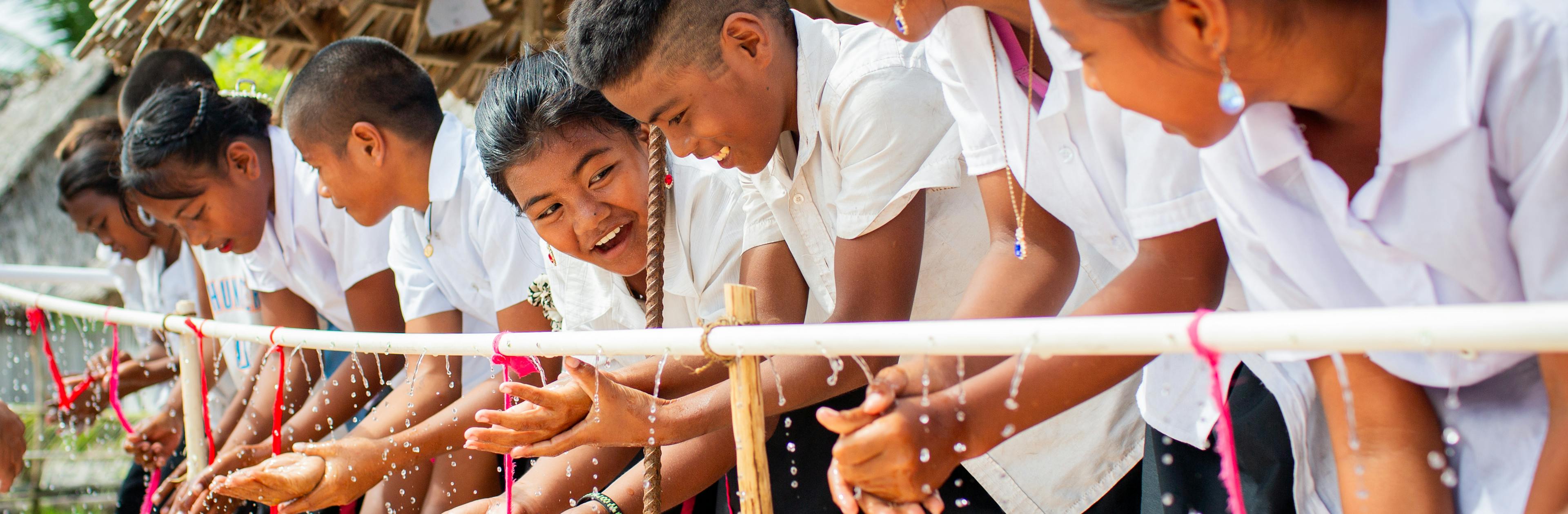 Children washing their hands using a tippy tap.