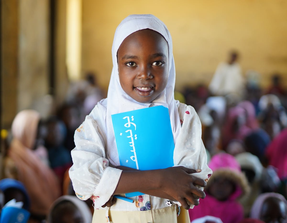 seven-year-old Aya stands in a classroom with her UNICEF exercise book at Dabba Nayra village school in Tawila, North Darfur