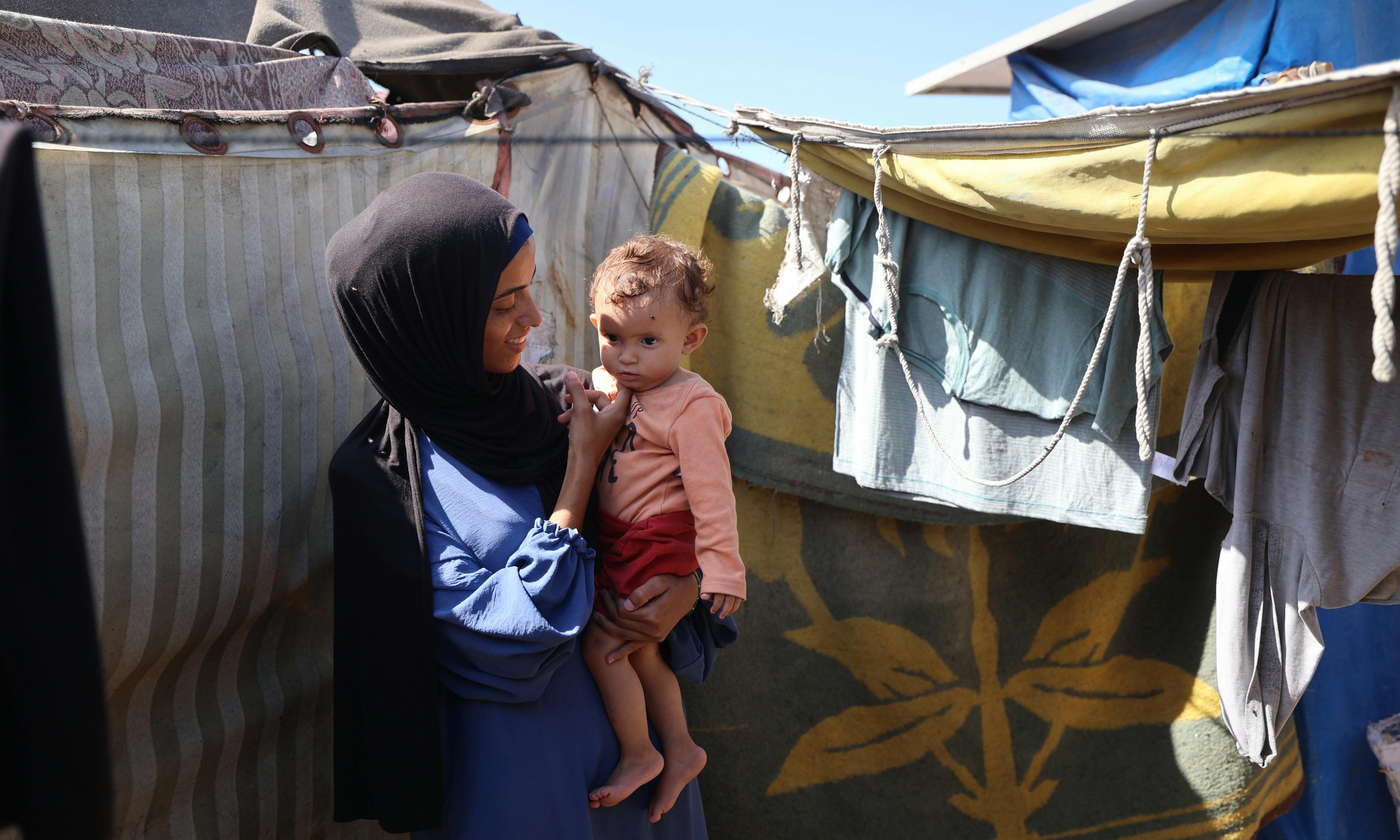 Rania holds her daughter Lareen outside their makeshift tent in Al-Mawasi in the Gaza strip.