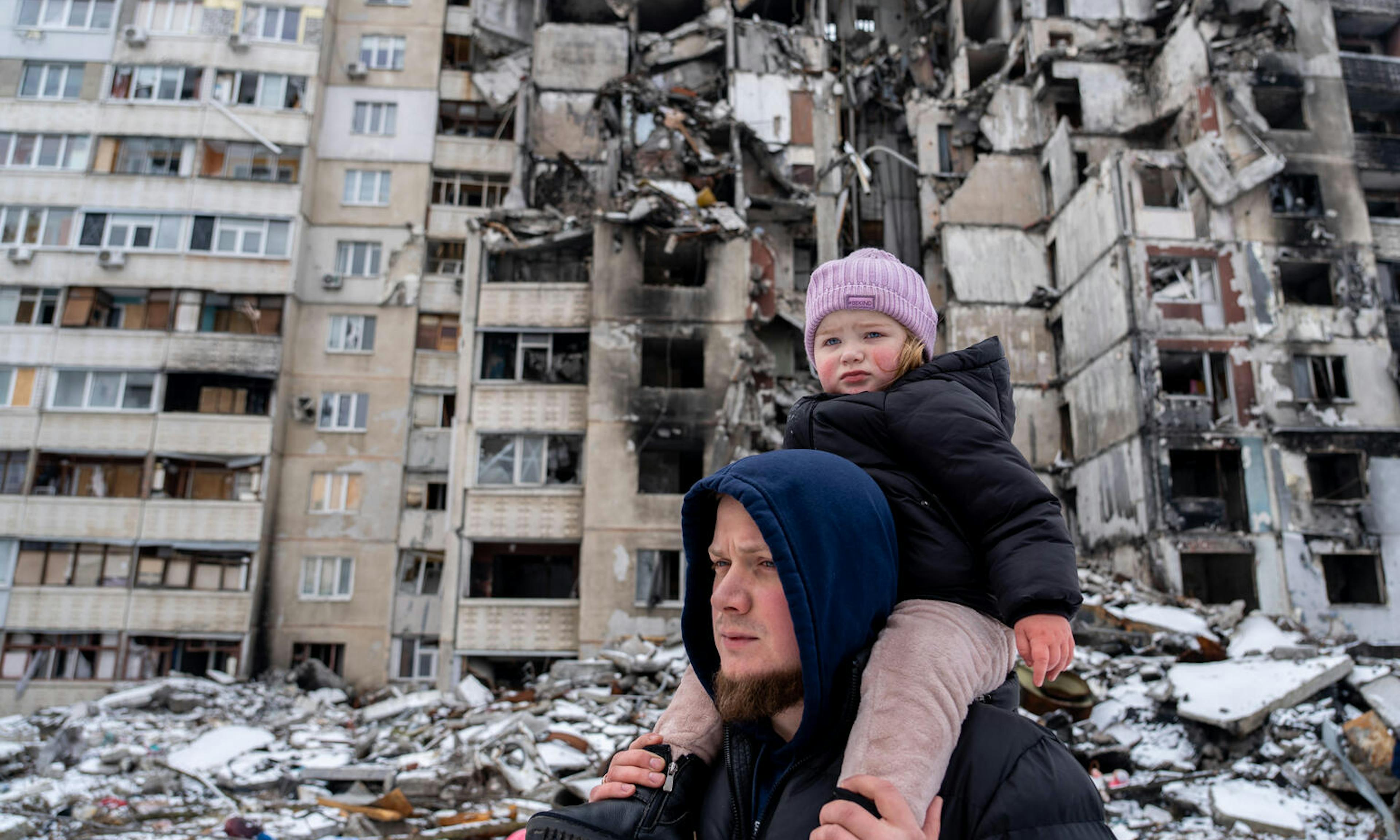 A child and her father walk next to a bombed out building in Ukraine