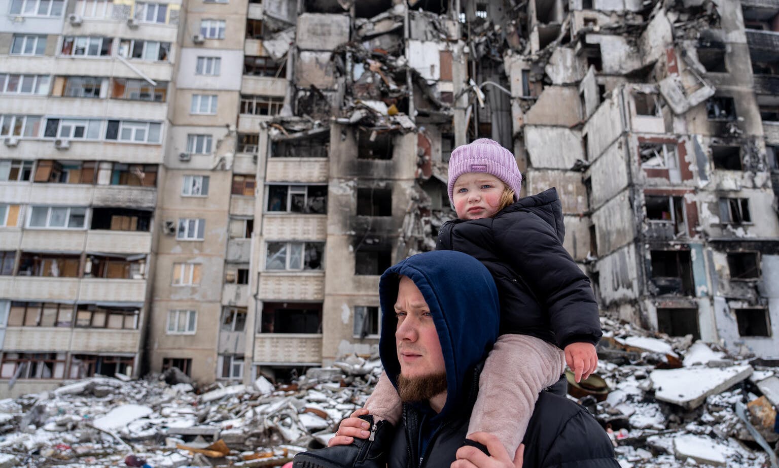 A child and her father walk next to a bombed out building in Ukraine