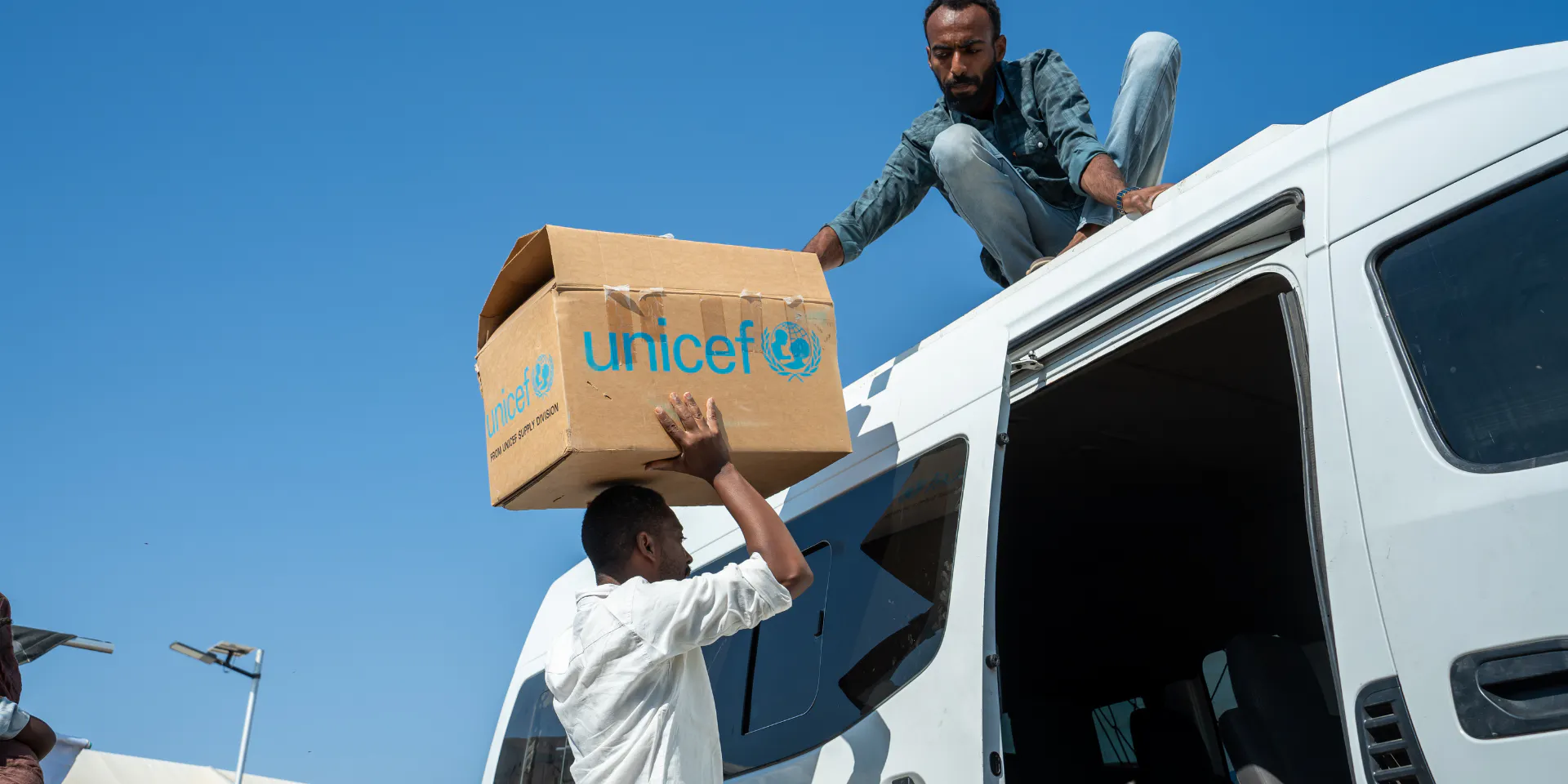 UNICEF-aid-workers-pass-supply-box-from-a-van