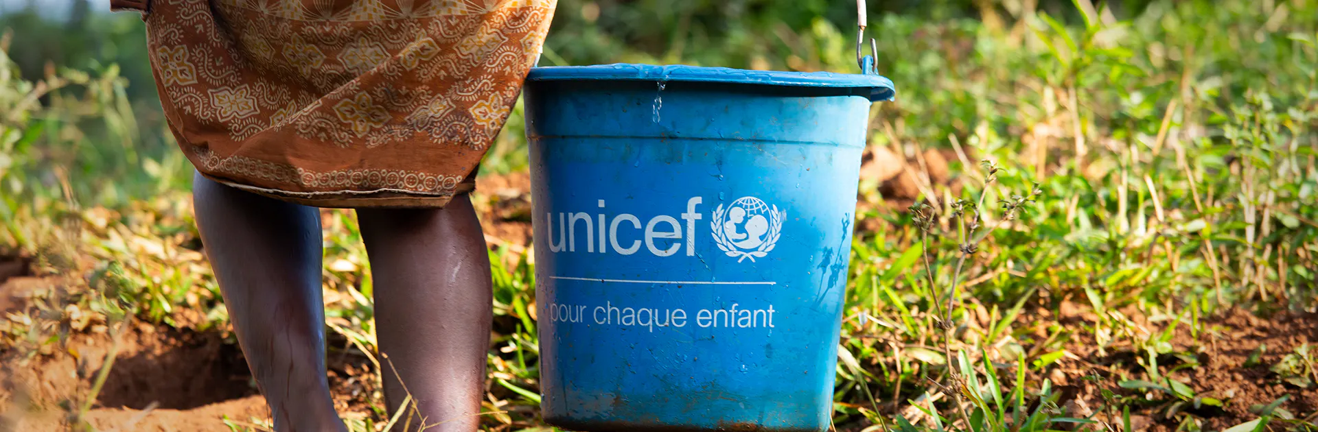 A women carrying a UNICEF supplied bucket to carry water from a water source back to her family.