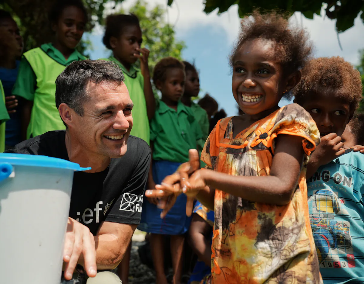 Dan Carter smiles as a young girl in the Pacific washes her hands with clean water provided through initiatives by UNICEF Aotearoa and the support of the DC10 Fund.