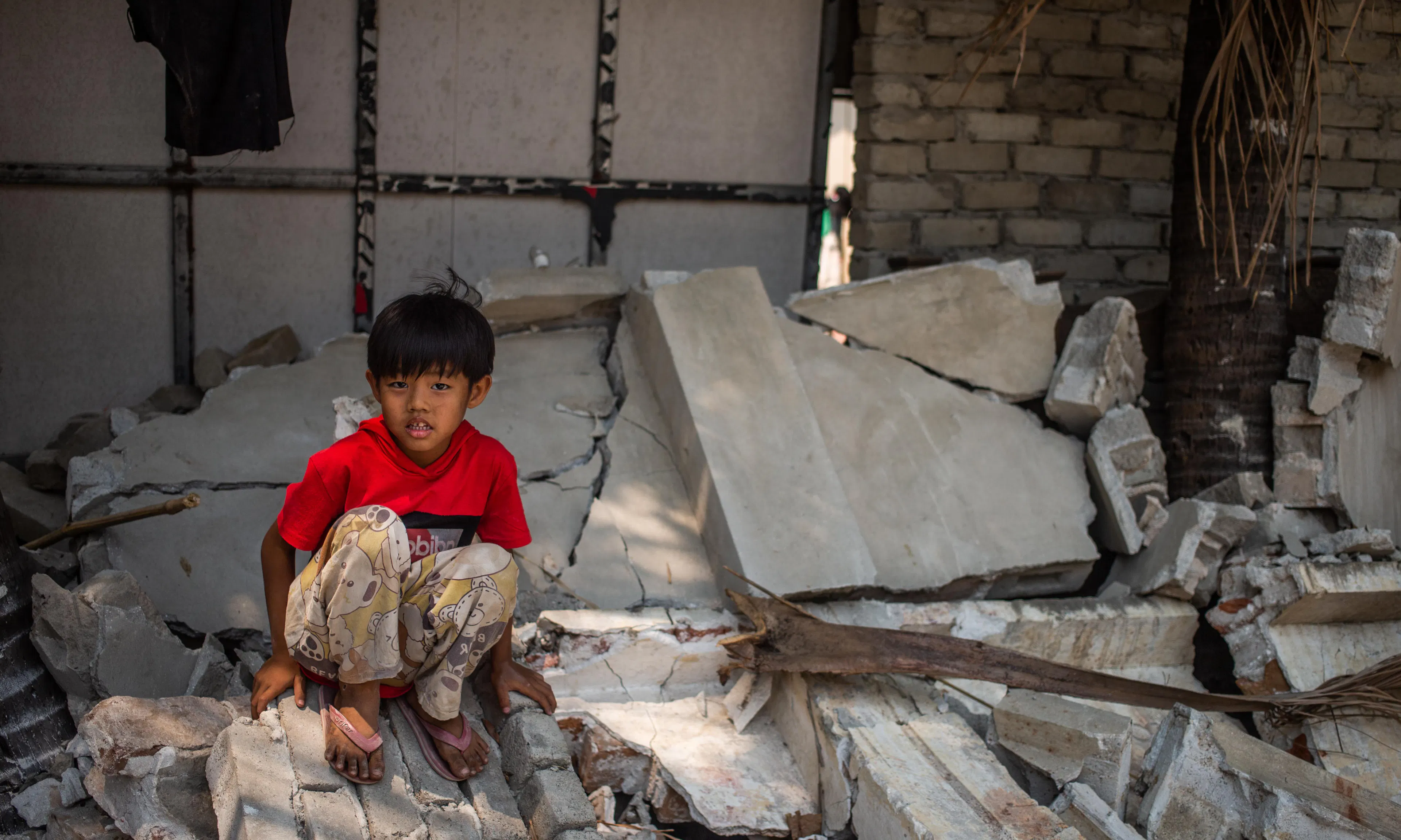 On 2 April 2025 in Myanmar, a boy sits on a piece of a collapsed wall of the Aye Thukha Community Hall in the Mahar Aung Myay Ward of Mandalay, several days after the devastating earthquake.