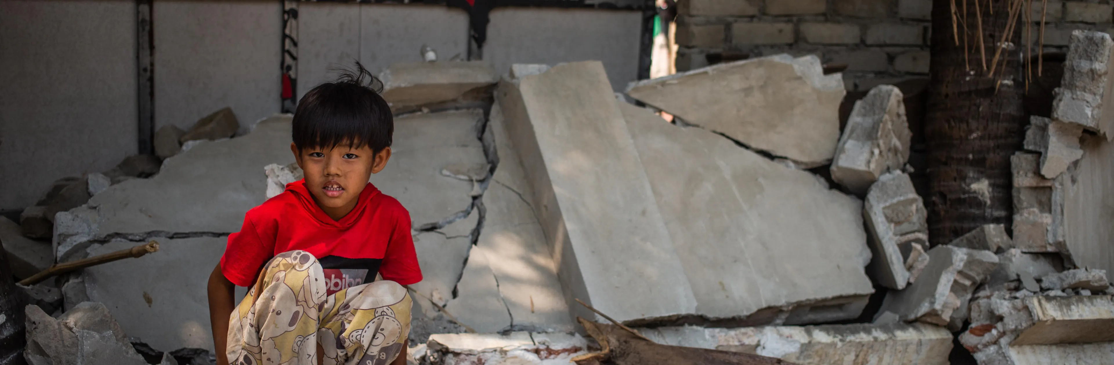 On 2 April 2025 in Myanmar, a boy sits on a piece of a collapsed wall of the Aye Thukha Community Hall in the Mahar Aung Myay Ward of Mandalay, several days after the devastating earthquake.