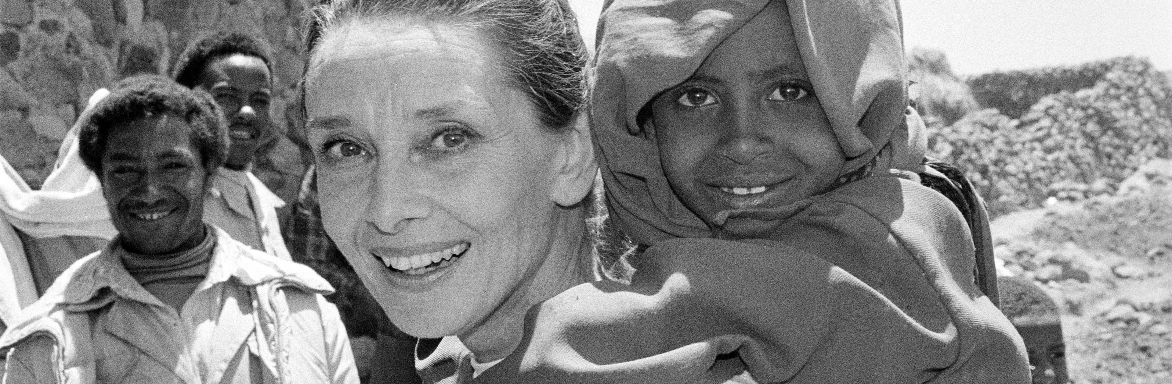 UNICEF Goodwill Ambassador Audrey Hepburn smiles as she carries a child on her back, in the northern town of Mehal Meda in Shoa Province. Ms. Hepburn was visiting a food distribution centre in the town.