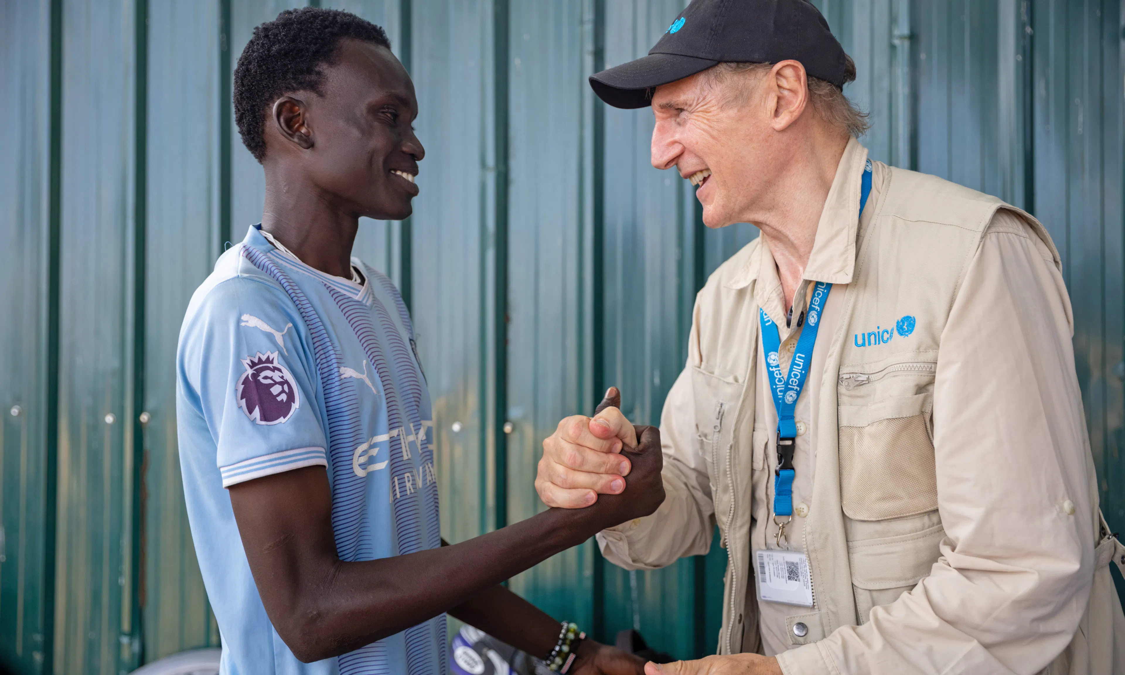 On 20 October 2025 in South Sudan, UNICEF Goodwill Ambassador Liam Neeson locks hands with Alan Rugumoch, 20, at the Gredo Youth Centre in Juba. The site provides a safe space for young people from unstable backgrounds, including those affected by gang violence and abuse.