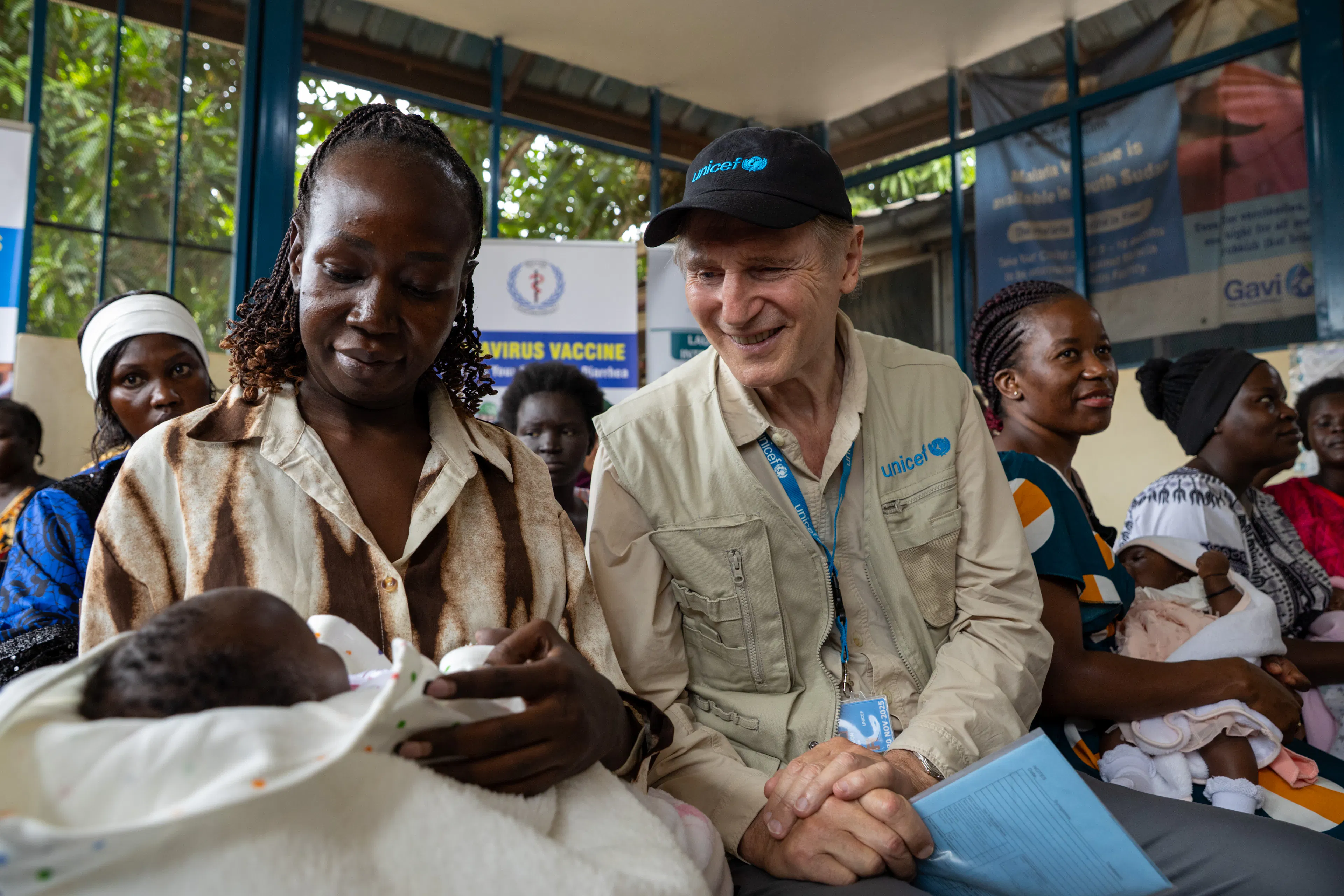 On 20 October 2025 in South Sudan, UNICEF Goodwill Ambassador Liam Neeson speaks to Magar Aweng, 32, who cradles her 1-month-old daughter, Ngor Awein, on her lap at the Al Sabbah Children’s Hospital in Juba. Ms. Aweng has brought her daughter to be vaccinated against polio.