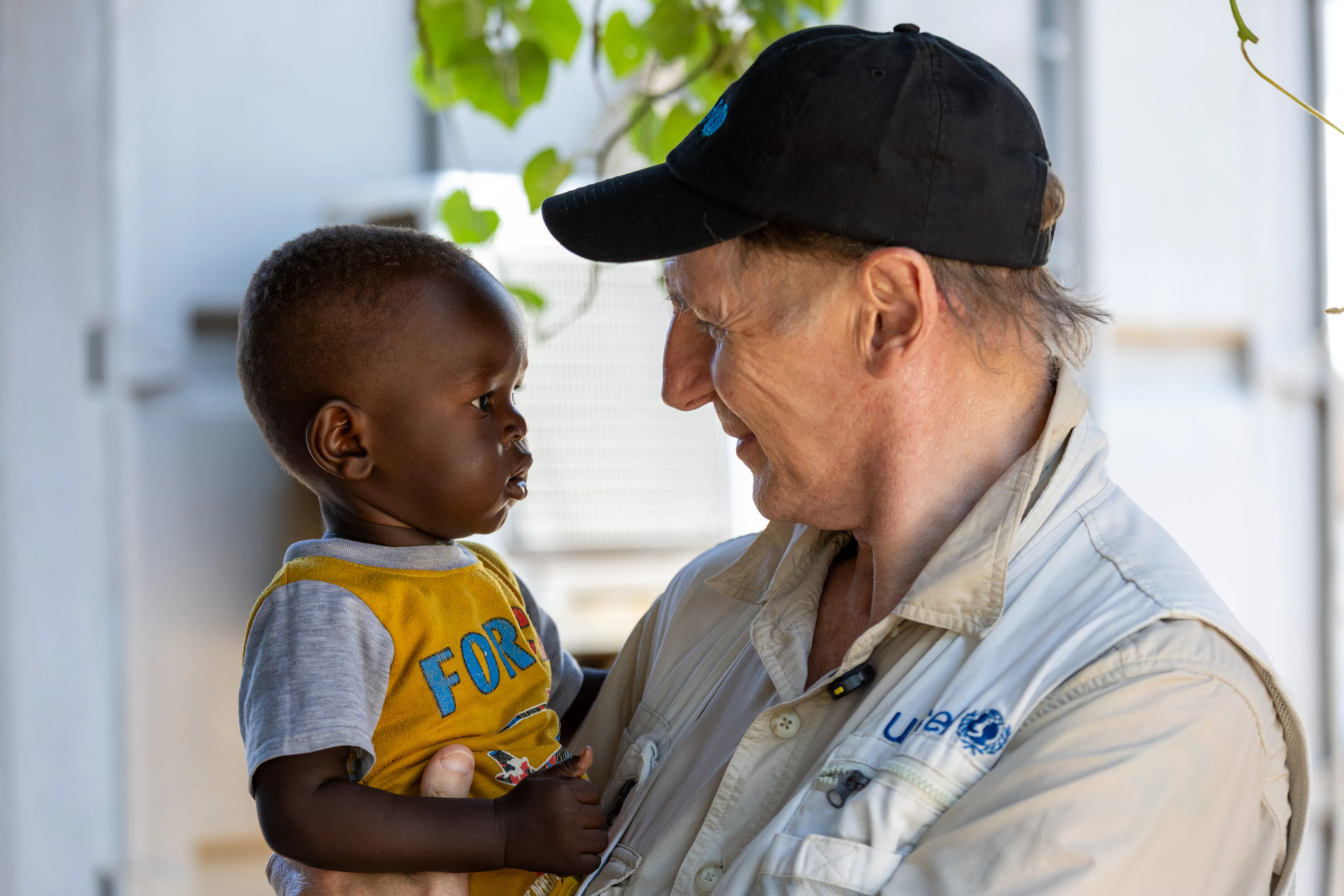 On 23 October 2025 at the nutrition ward of the Gumbo Primary Health Care Centre in Juba, South Sudan, UNICEF Goodwill Ambassador Liam Neeson holds 14-month-old Augustino Remezy, while Augustino’s mother, Emelda Pio (not pictured), 22, waits in line to receive money as part of a UNICEF-implemented cash transfer programme.