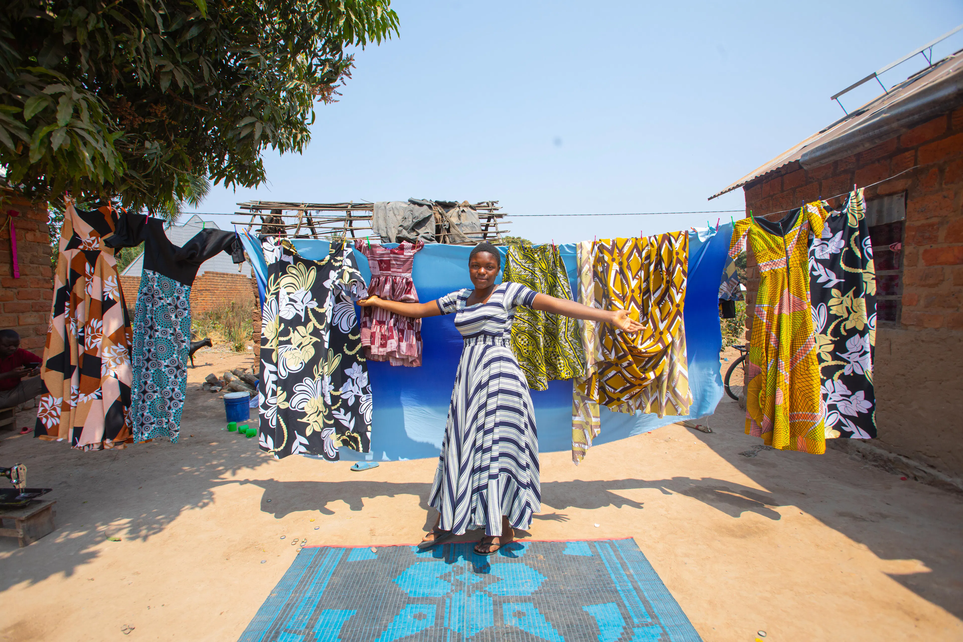 Antini Mahepa, 17, stands with her  fashion creations outside her home in the town of Uvinza, located in the Kigoma region of Tanzania.