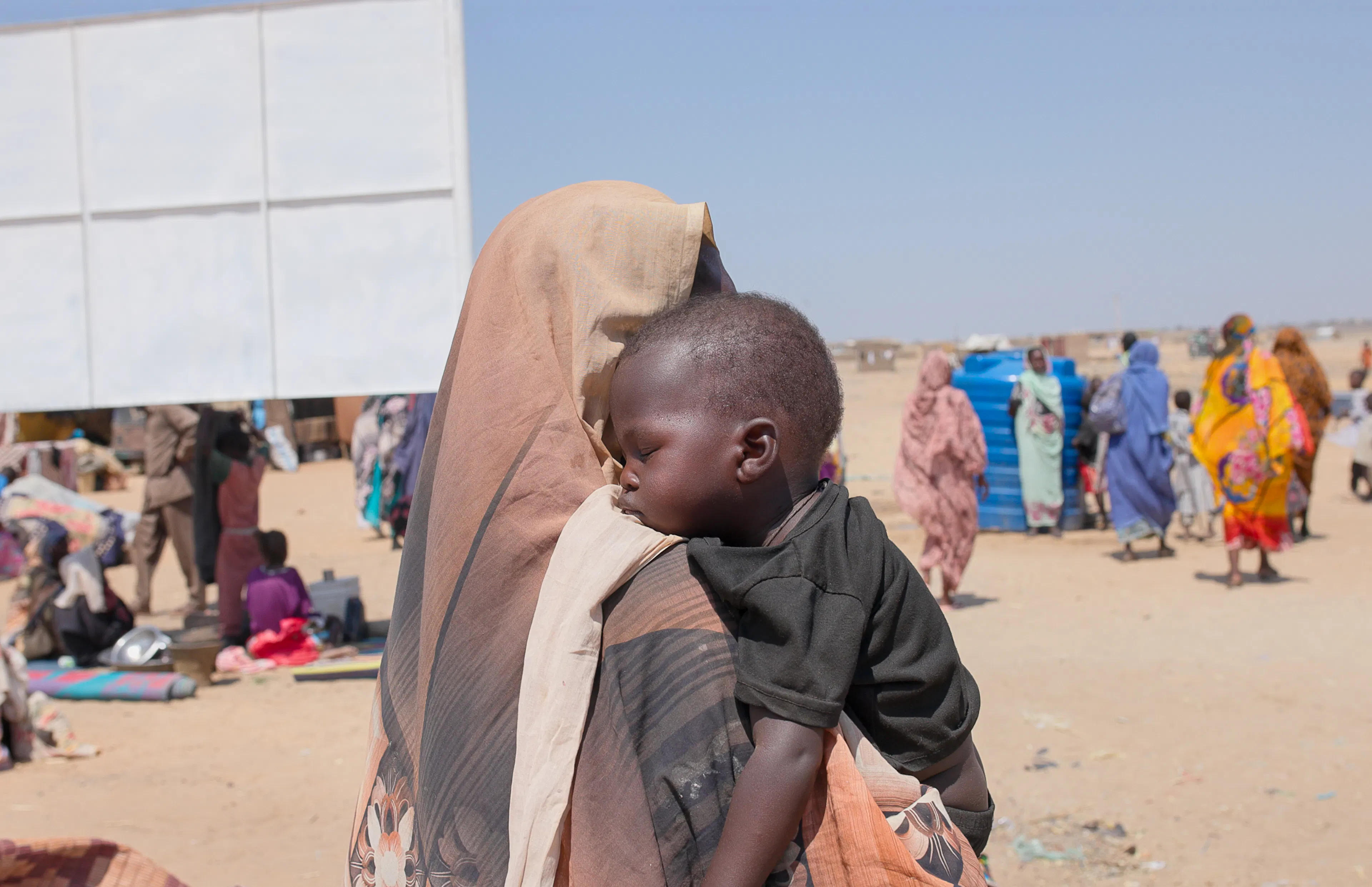 Halima carries her youngest two-year-old son Samsadeen upon arrival at Goz Alsalam IDP site in White Nile State.