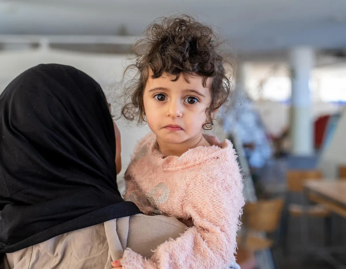 On 17 March 2026 in Lebanon, 2-year old Fatima is held by Fadak, 12, at Omar Faroukh school in Beirut, where hundreds of internally displaced people are currently staying after fleeing violence.